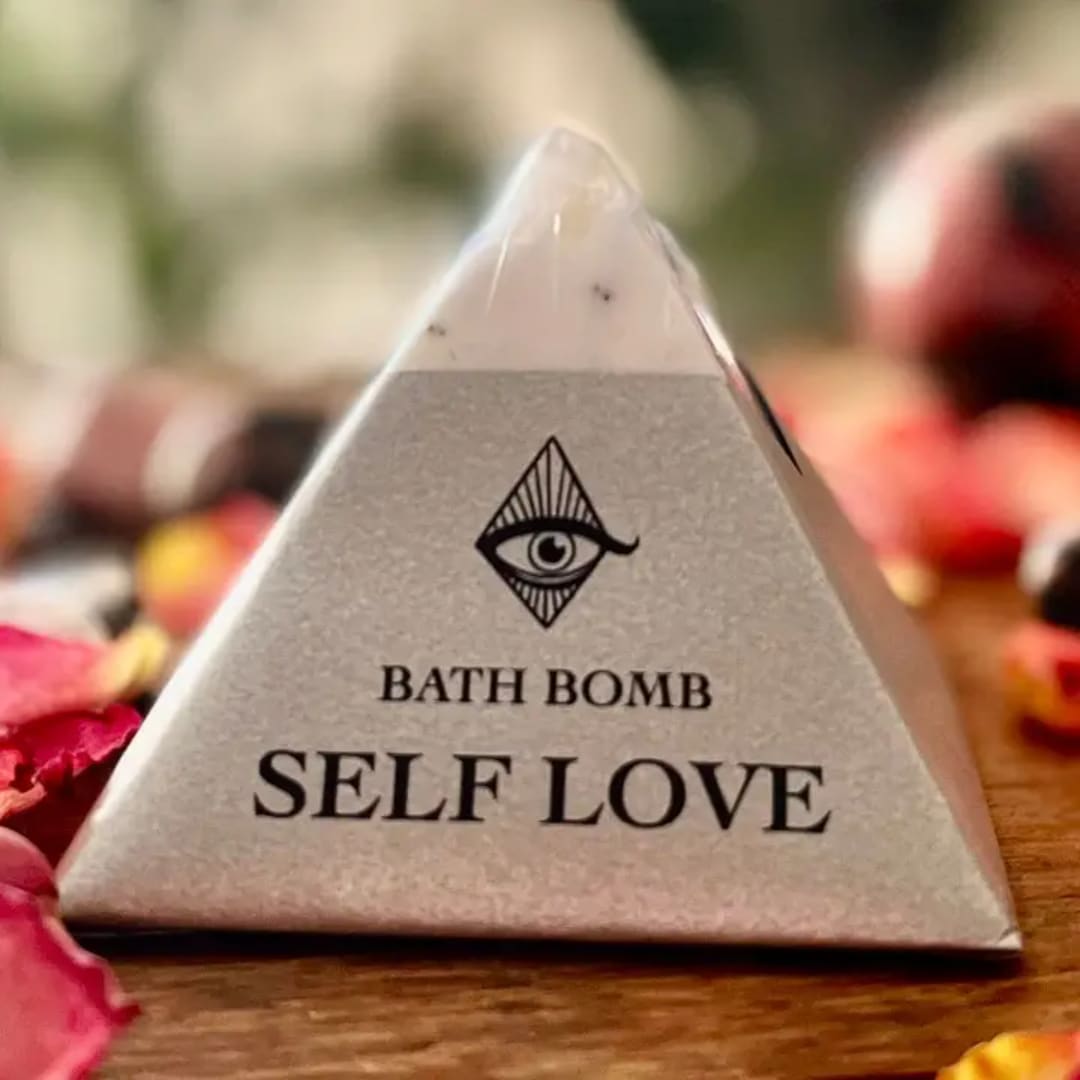 Triangular bath bomb package labeled Self Love on a wooden surface