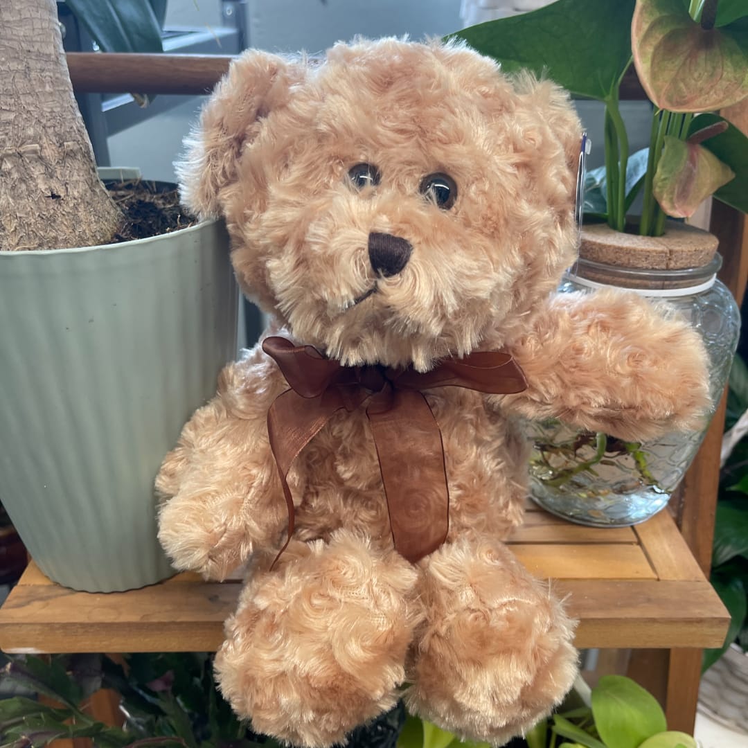 Teddy bear with a brown ribbon sitting beside potted plants