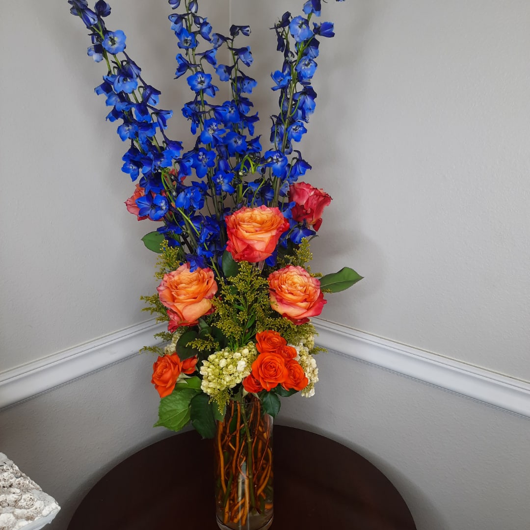 Tall bouquet of blue flowers and orange roses in a glass vase