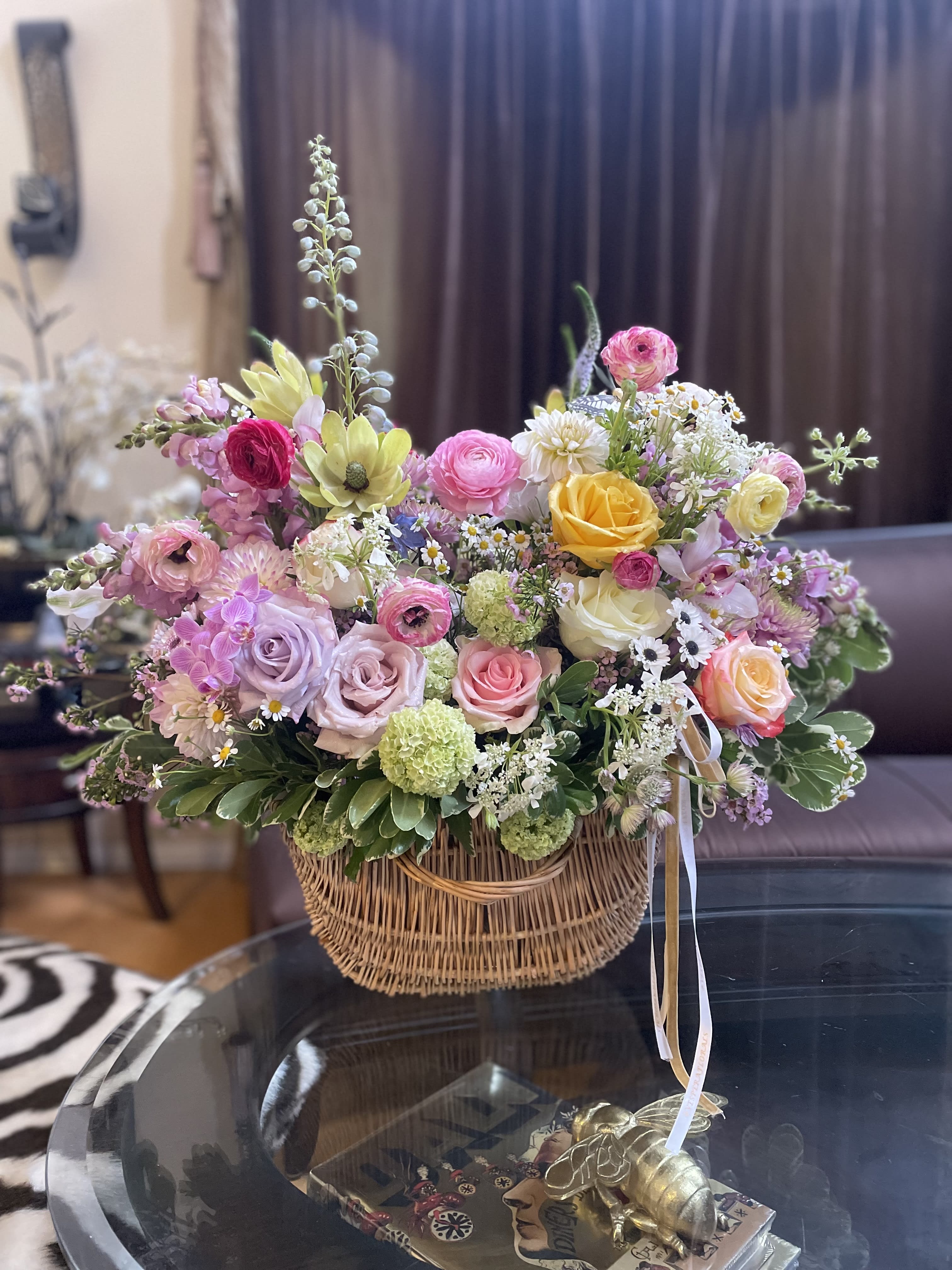 Mixed pastel flower arrangement in a wicker basket with ribbon ties