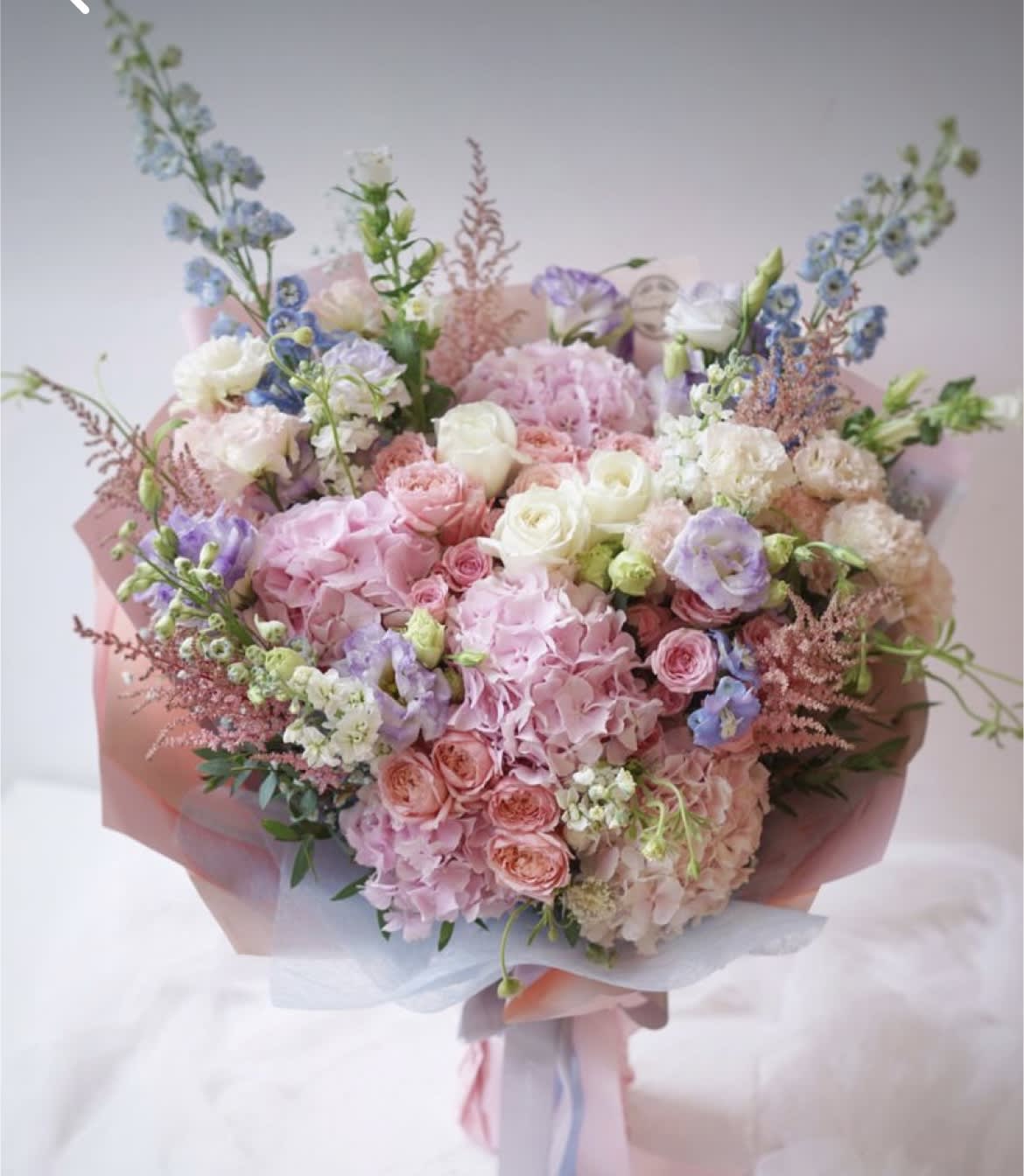 Large pastel bouquet of pink, white, and lavender flowers wrapped in pink paper