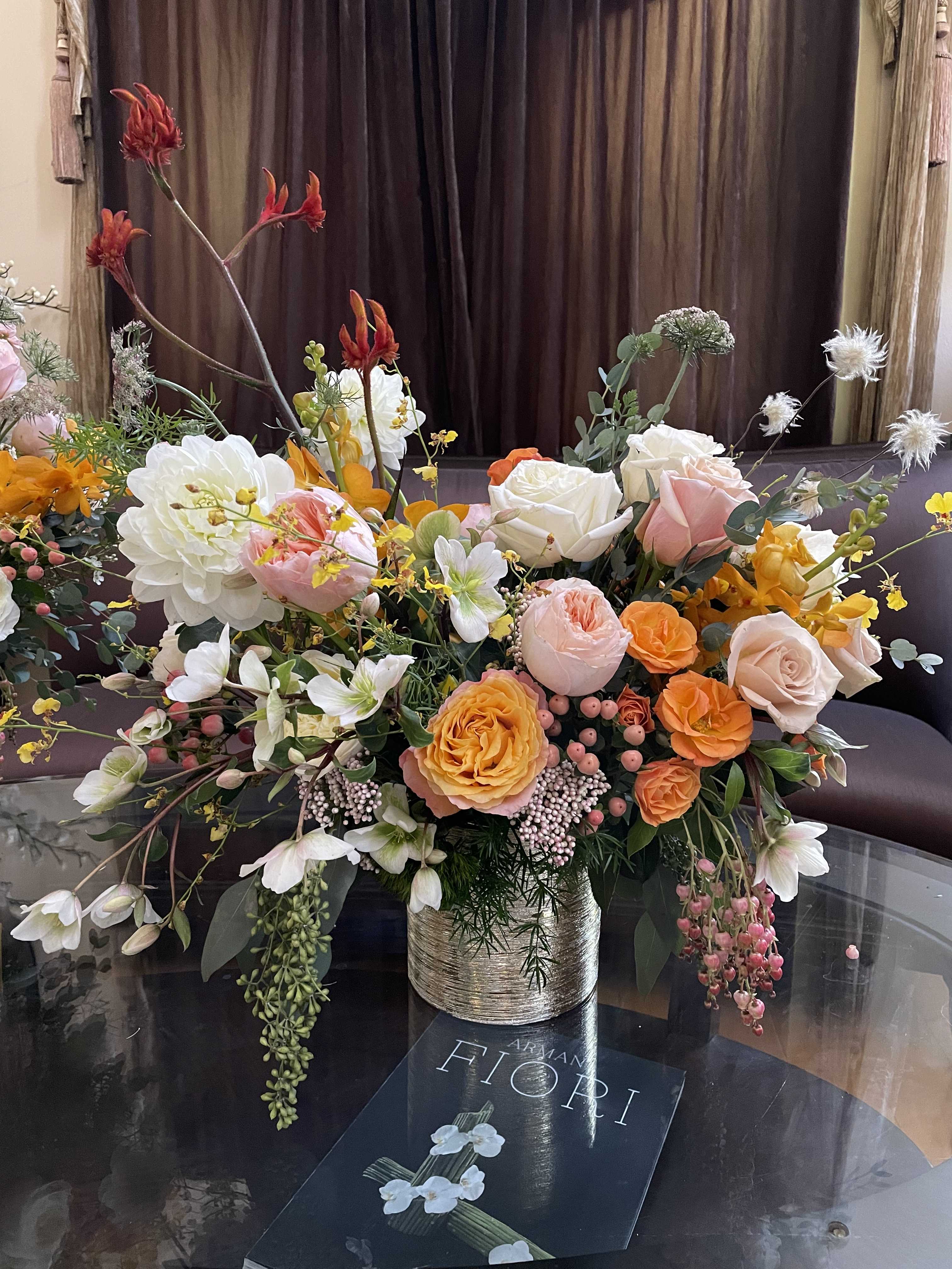 Large mixed bouquet of peach, white, and orange flowers in a metallic vase
