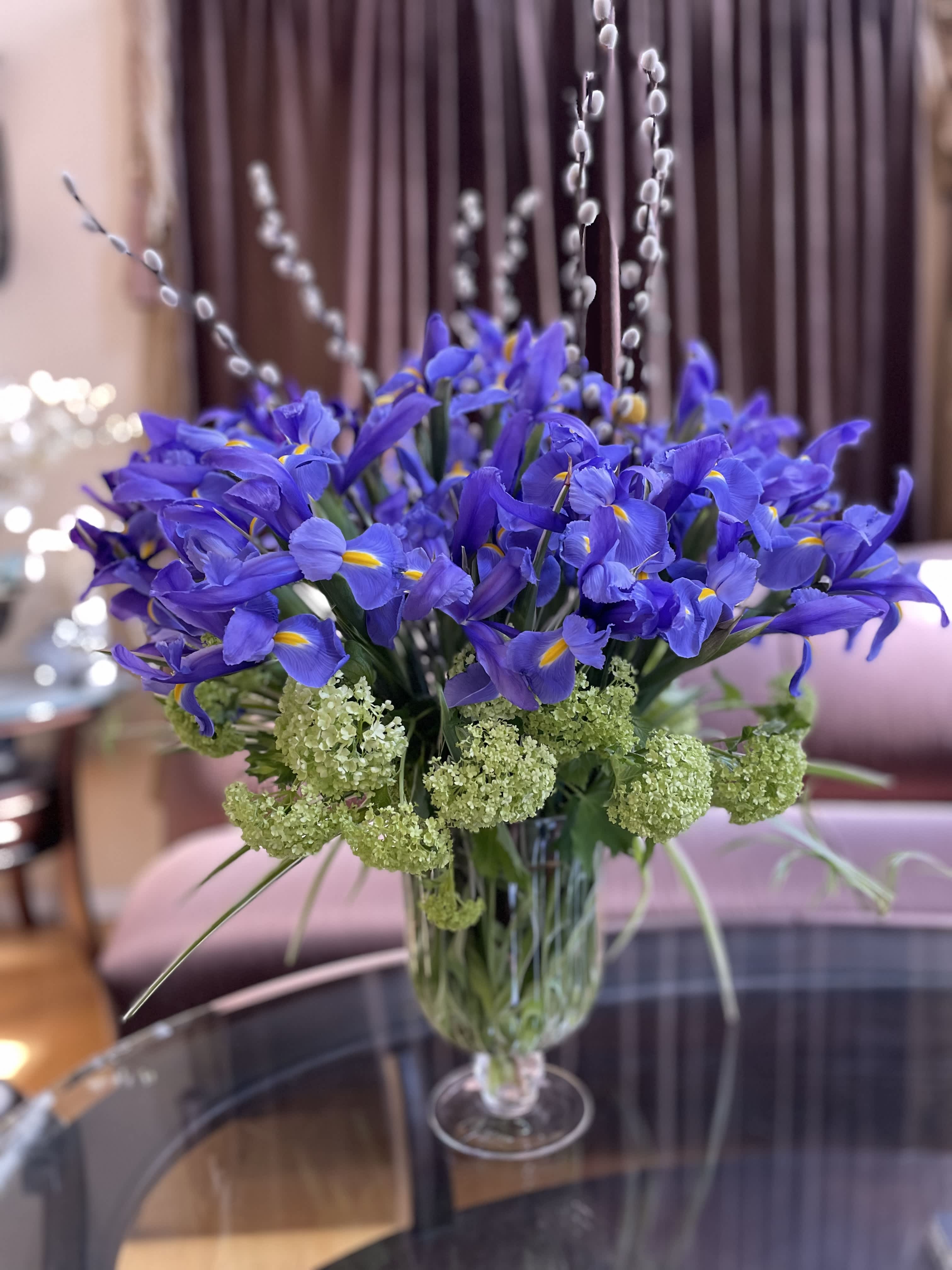 Blue iris bouquet in a clear glass vase with green filler flowers
