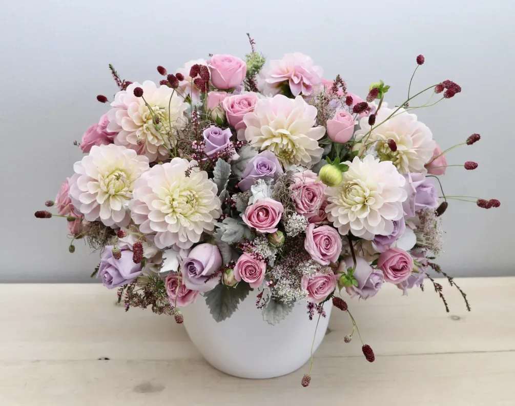 Pink and lavender roses with pale dahlias in a white vase