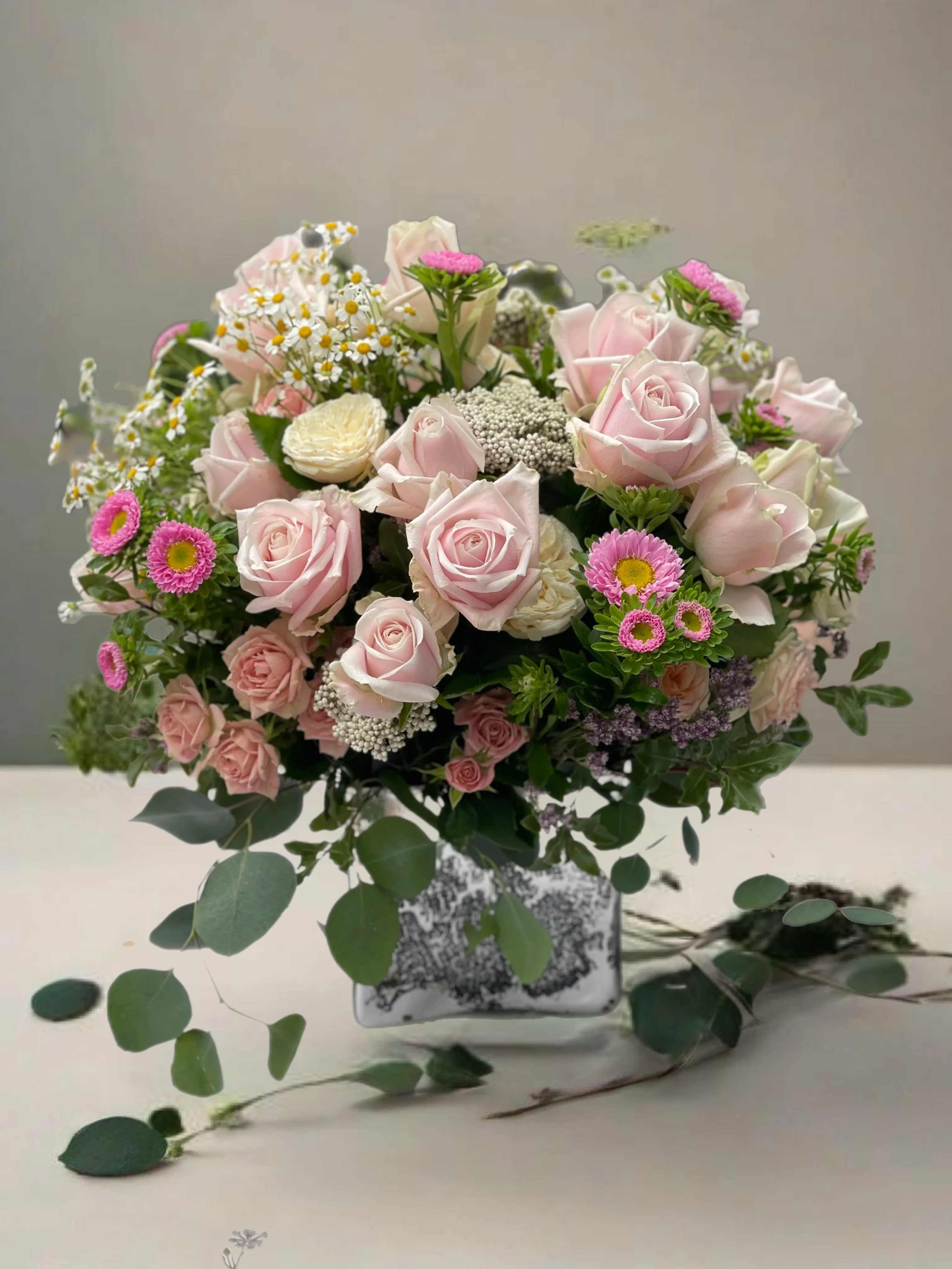 Pink roses and small daisies arranged in a square glass vase
