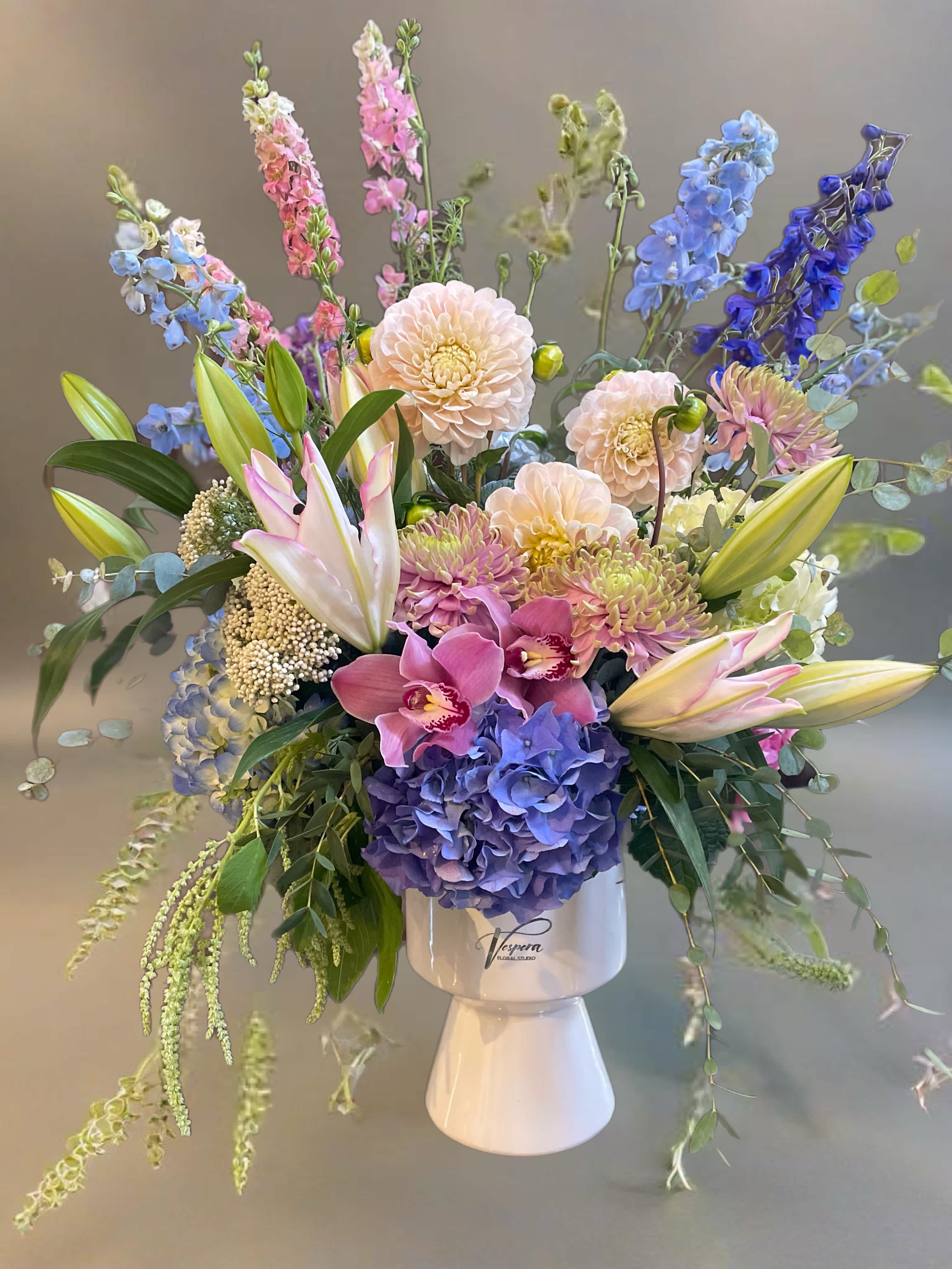 Mixed bouquet of pastel and blue flowers in a white pedestal vase