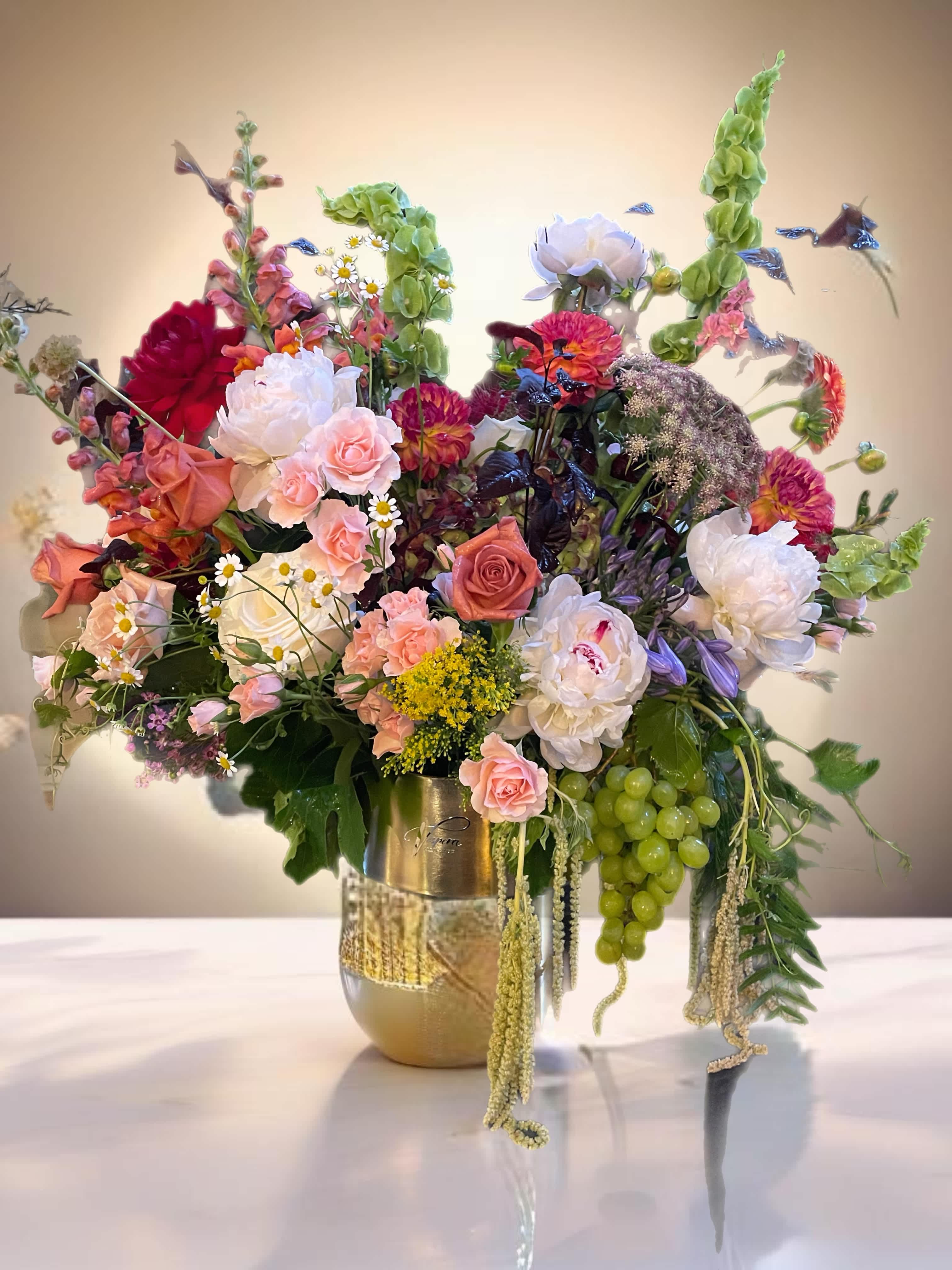 Large mixed floral arrangement in a gold vase with pink, white, and green blooms