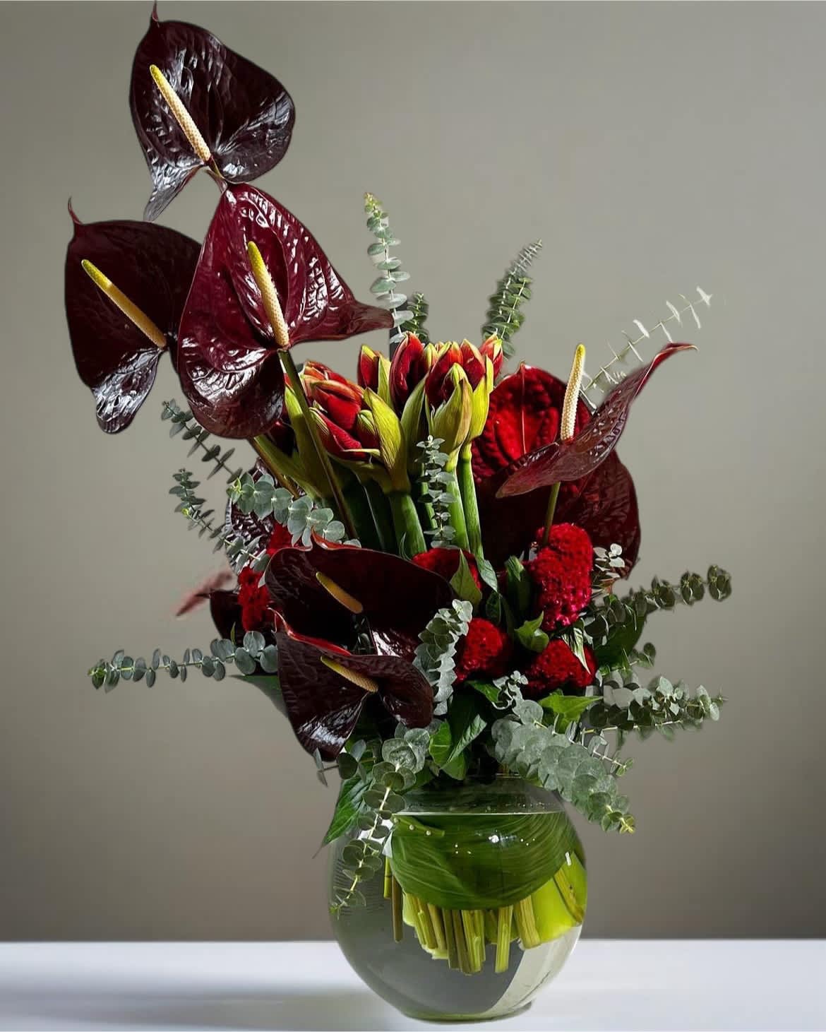 Dark red anthuriums and red flowers in a glass vase with eucalyptus