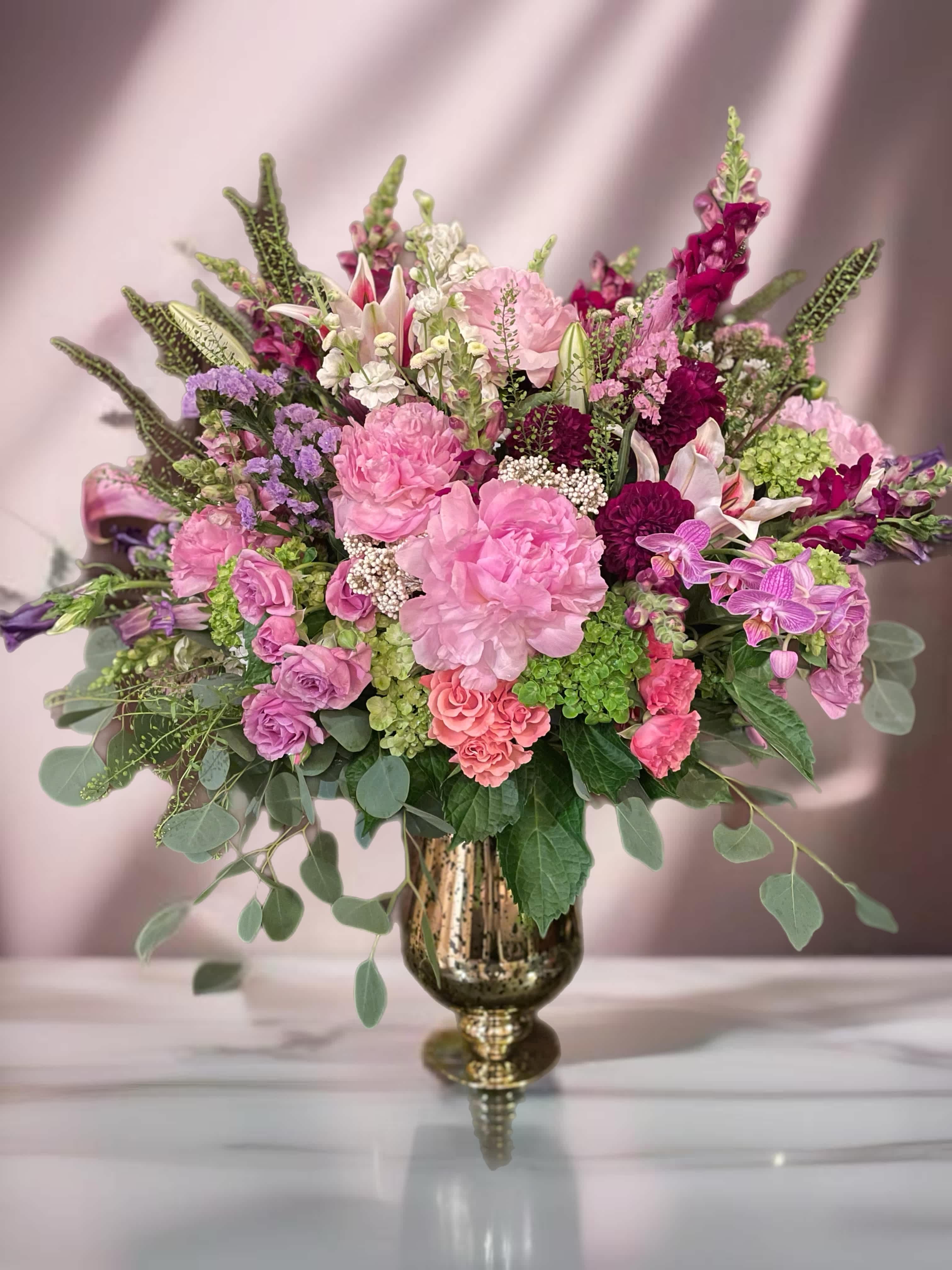 Large pink and purple floral arrangement in a gold vase