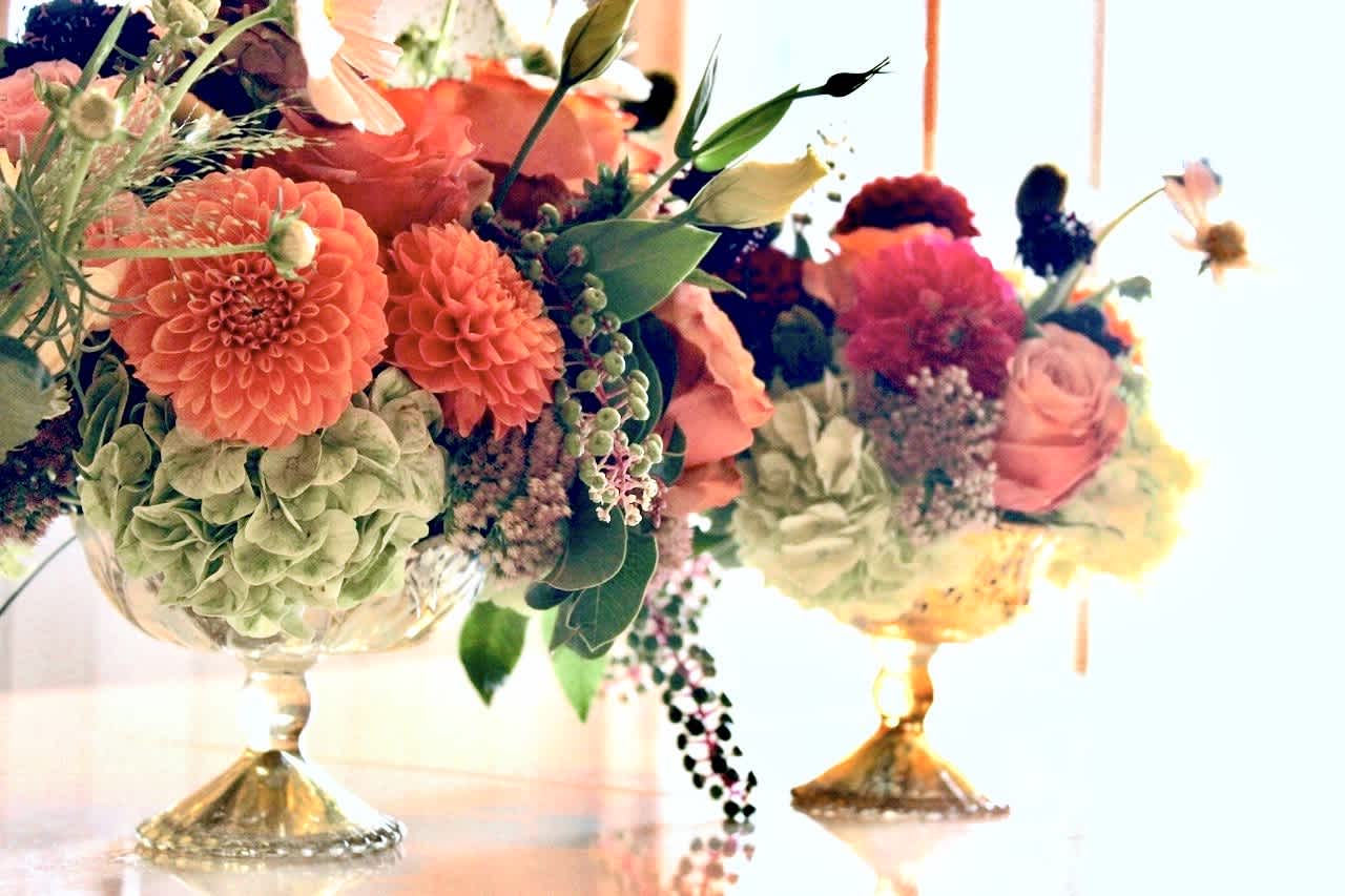 Two colorful floral arrangements in gold pedestal bowls