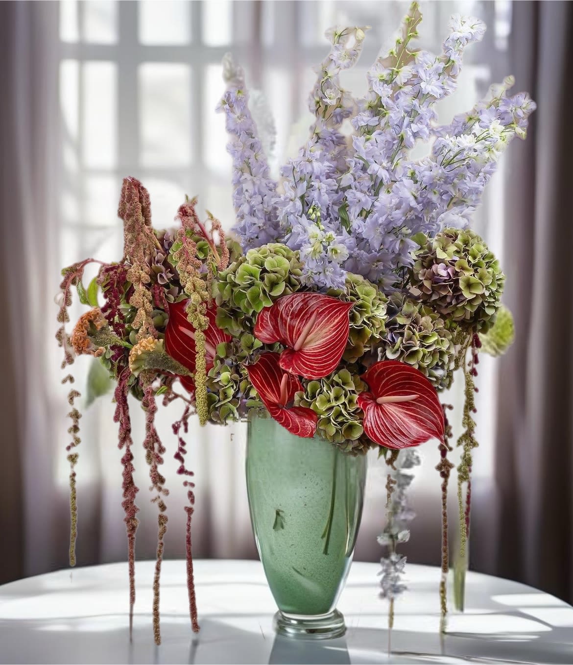 Tall floral arrangement in a green vase with red anthuriums and lavender blooms