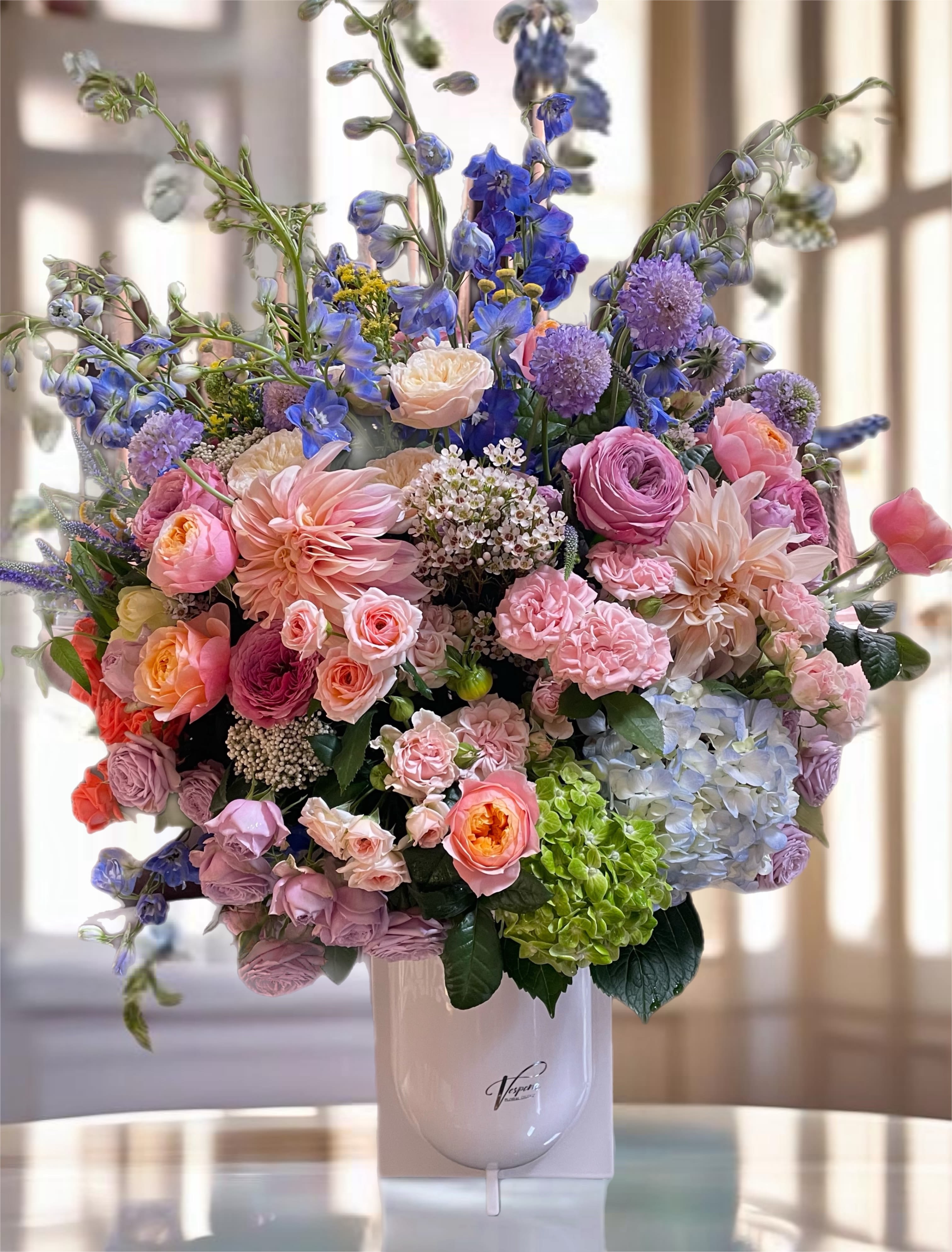Large pastel bouquet in a white vase with pink, blue, and purple flowers