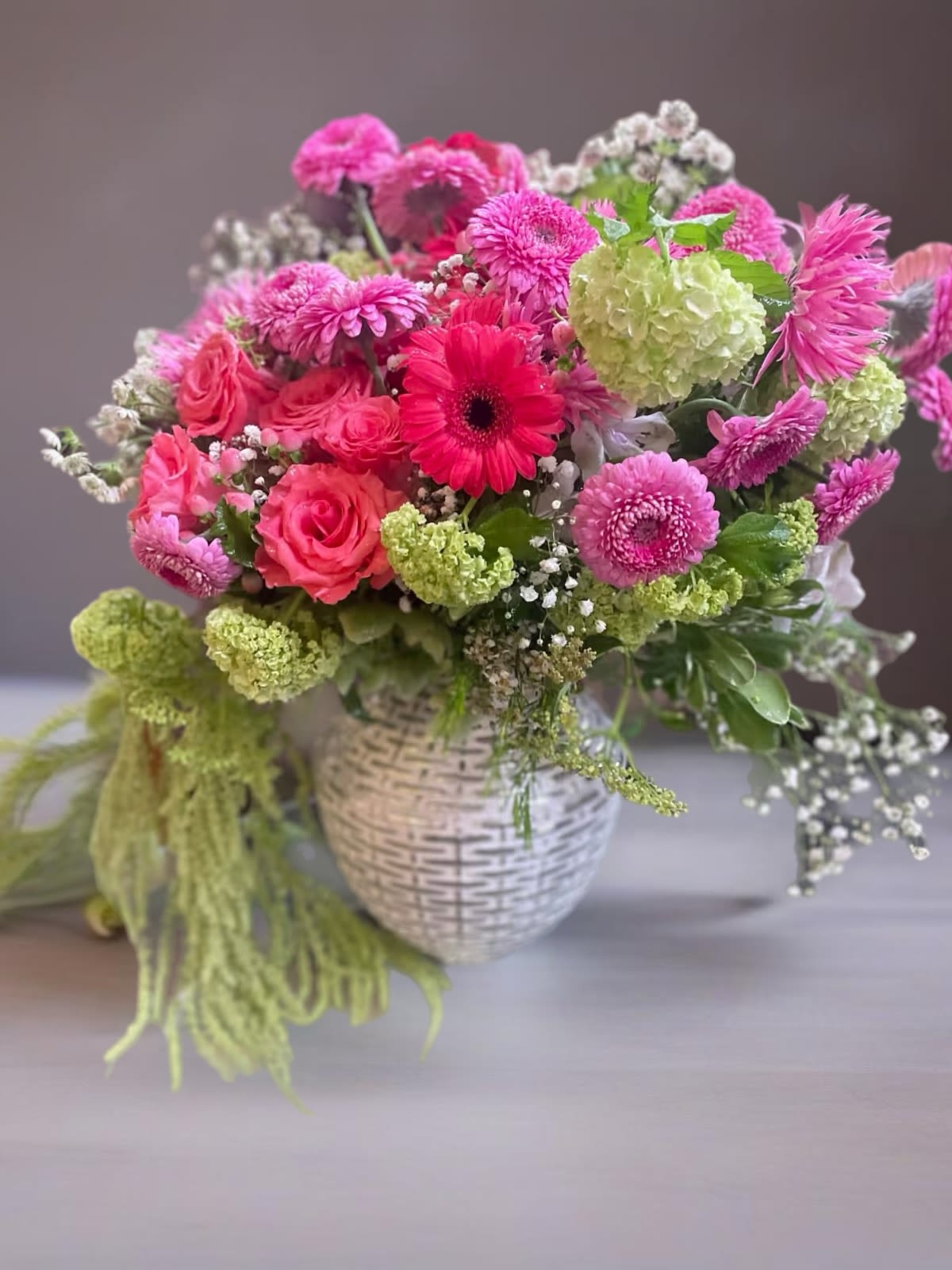 Pink and green mixed flower arrangement in a white woven vase