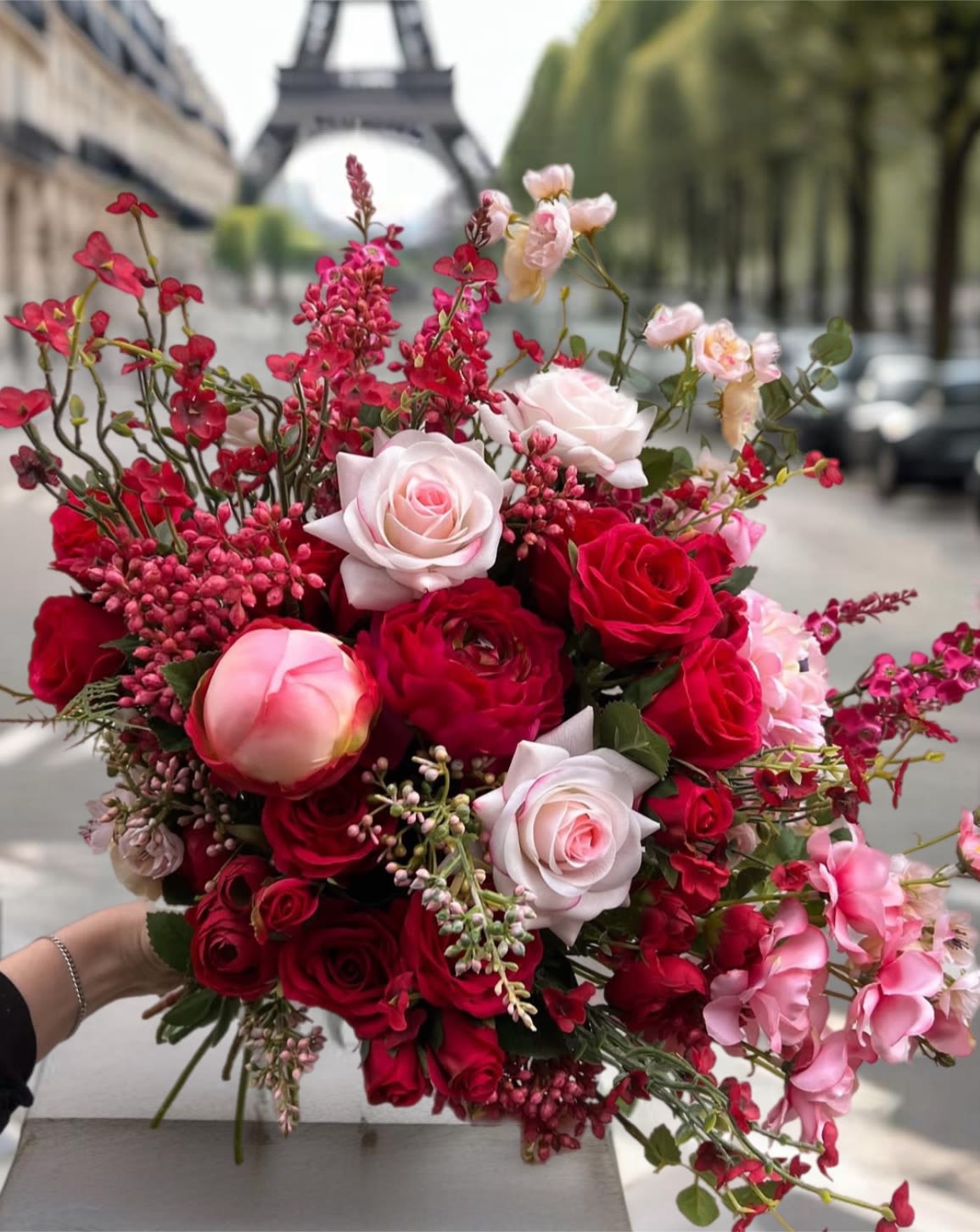 Handheld bouquet of red and blush roses with pink filler flowers