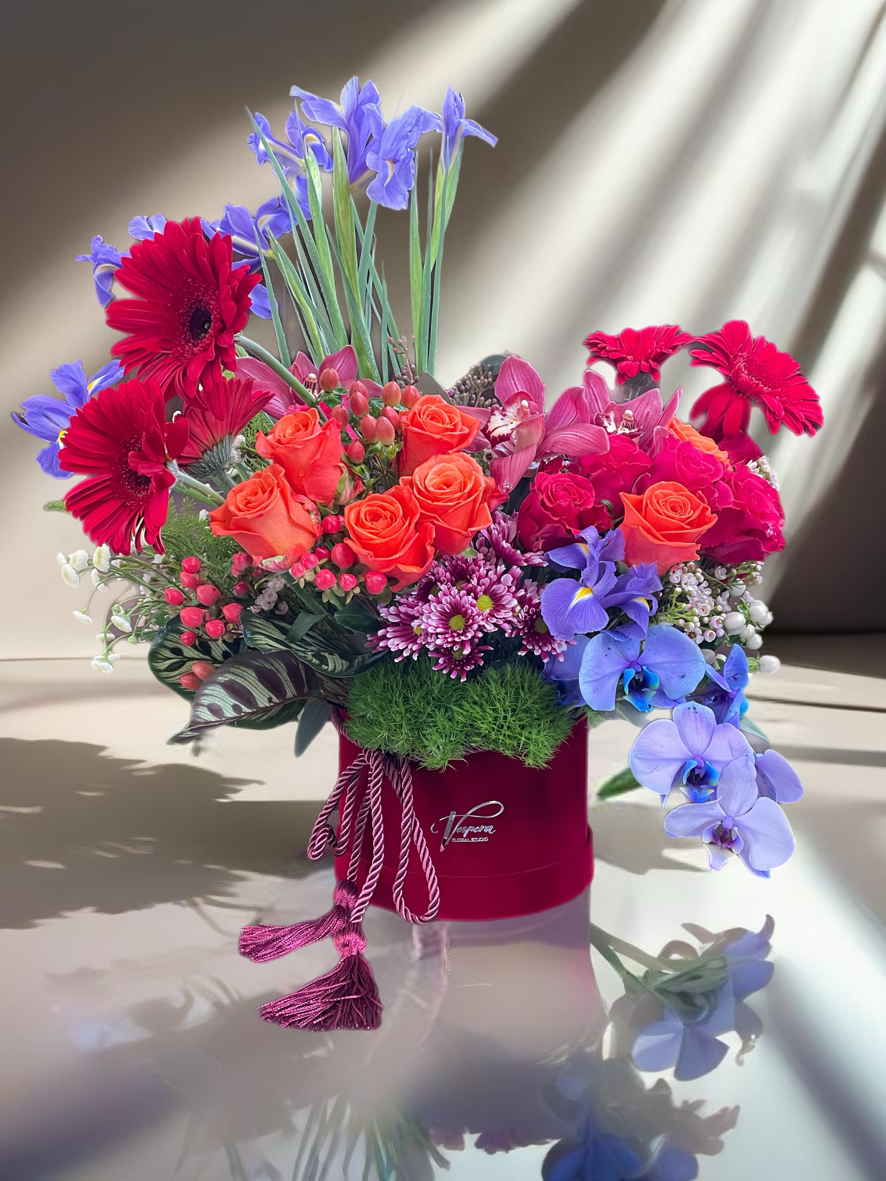 Mixed bouquet with orange roses, red gerberas, and purple orchids in a red hat box