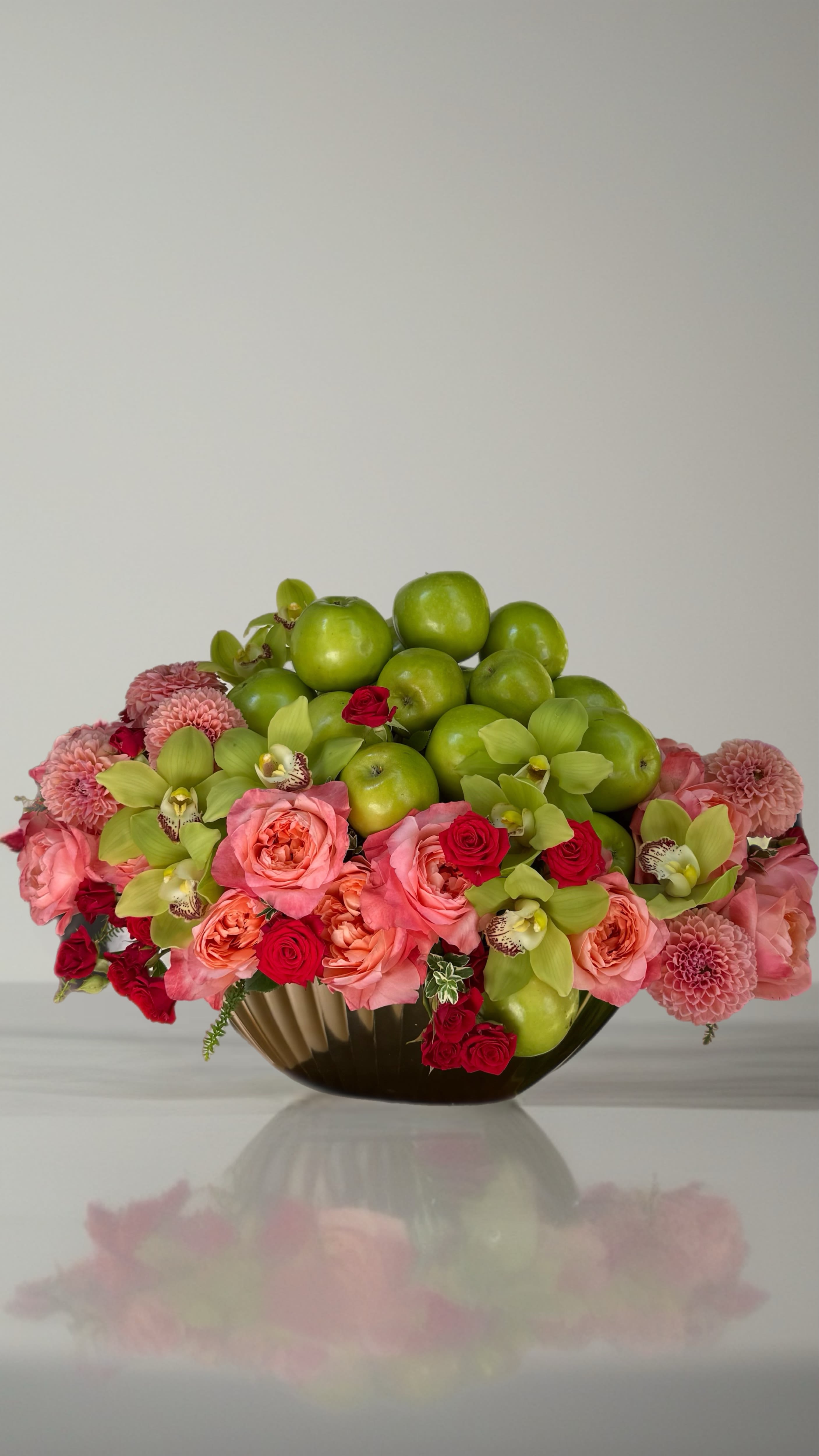 Pink and red floral arrangement with green apples in a low vase