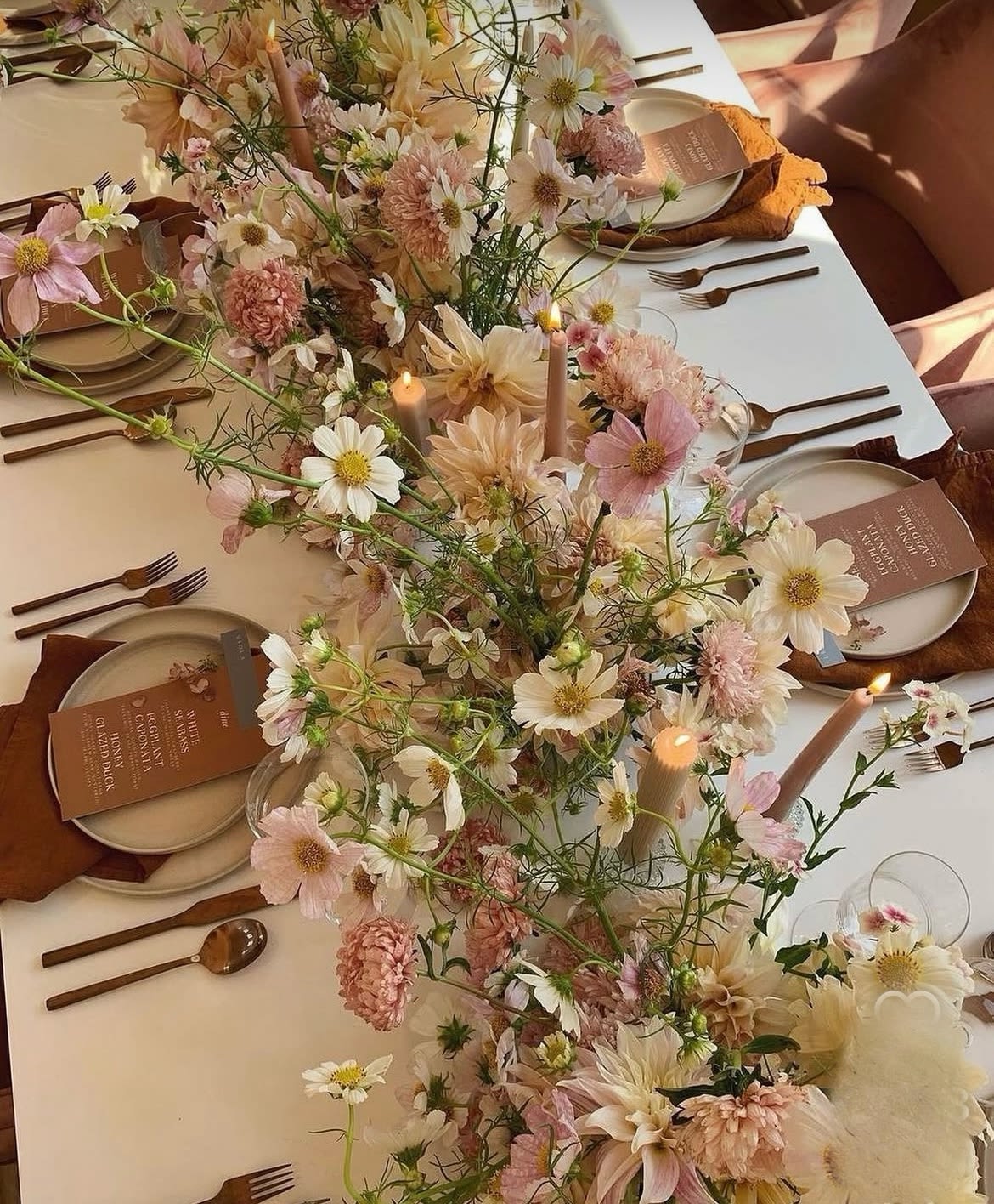 Pastel floral centerpiece running down a set table with candles and place settings