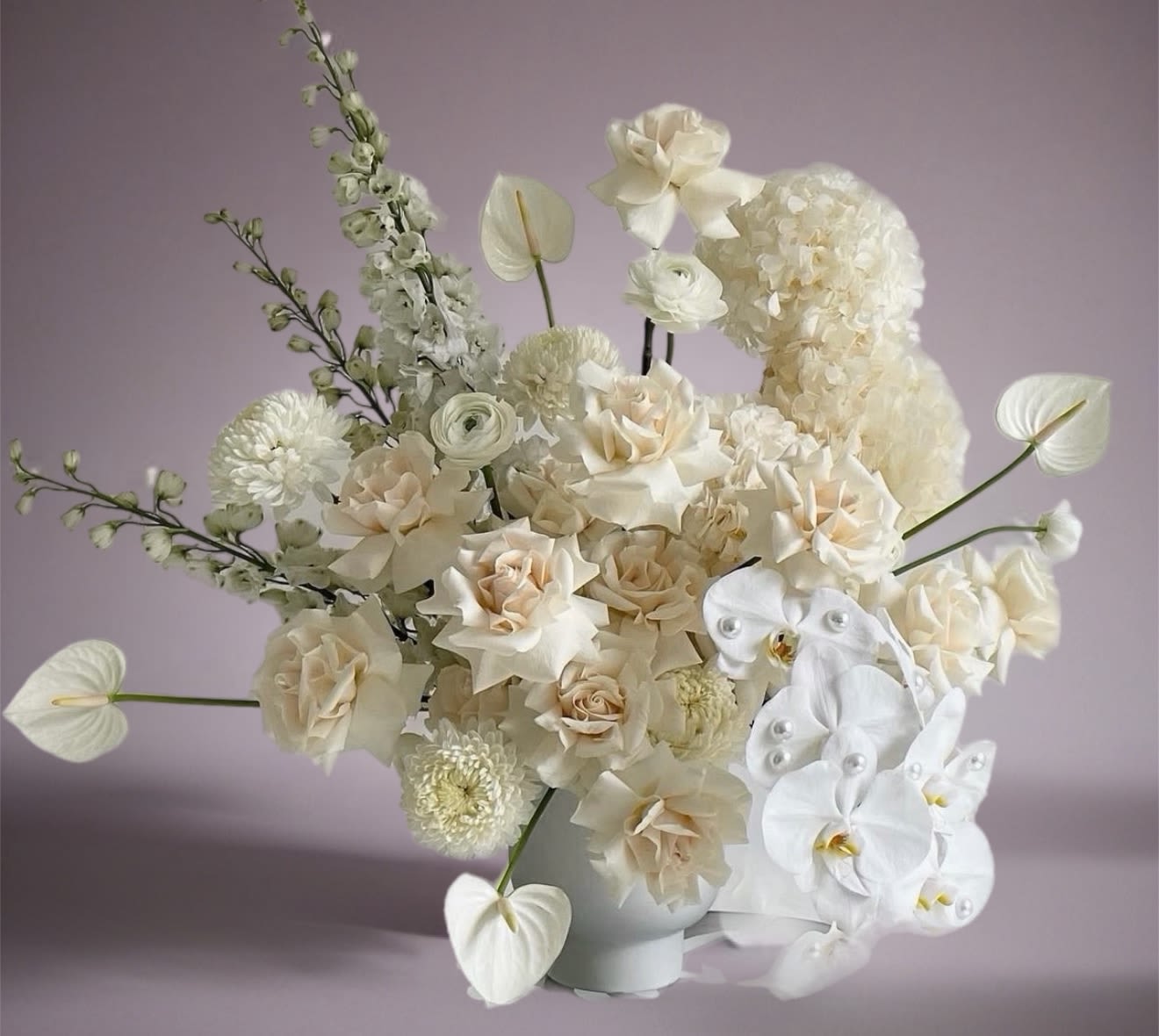 Cream and white floral arrangement in a white vase with orchids and roses
