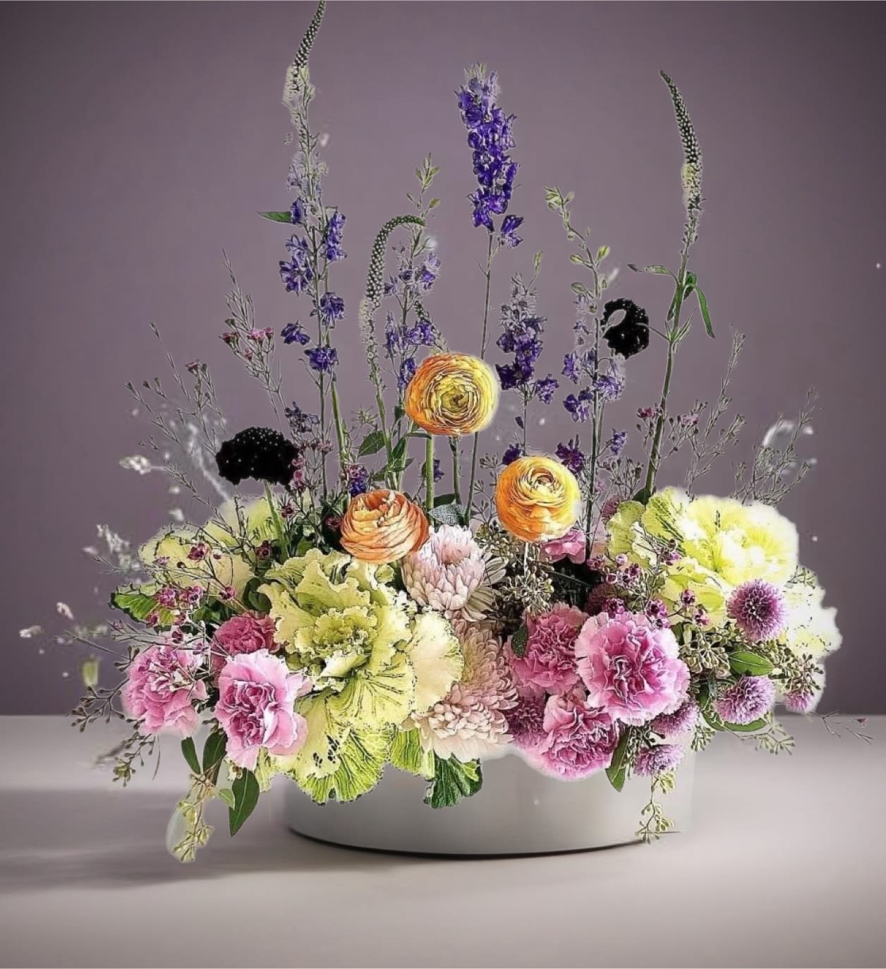 Mixed floral arrangement in a white bowl with pink, yellow, and purple blooms