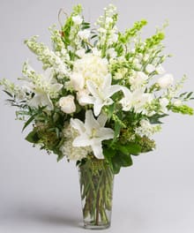 White lilies and pale blooms arranged in a clear glass vase