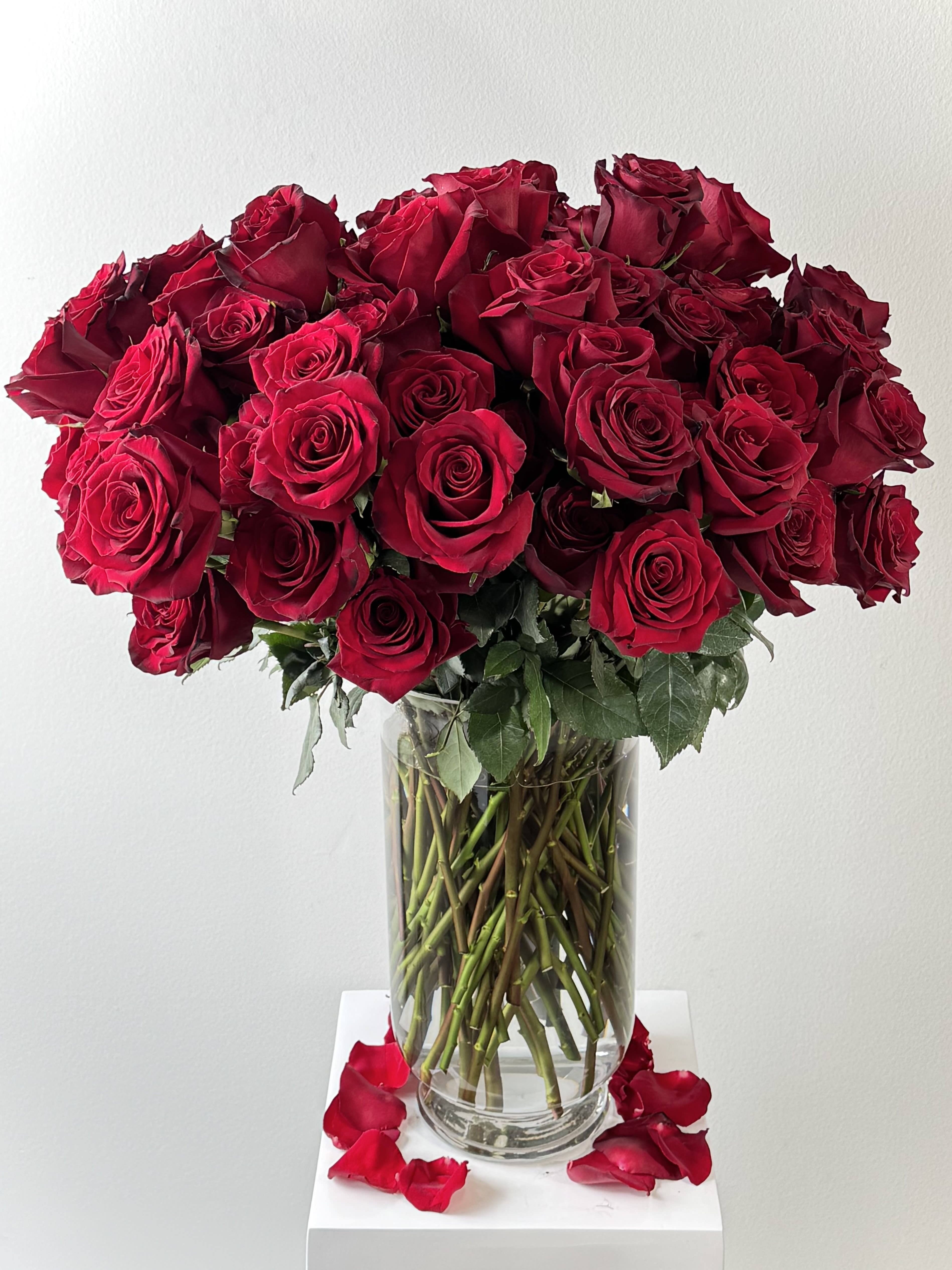 Bouquet of red roses in a clear glass vase with petals around the base