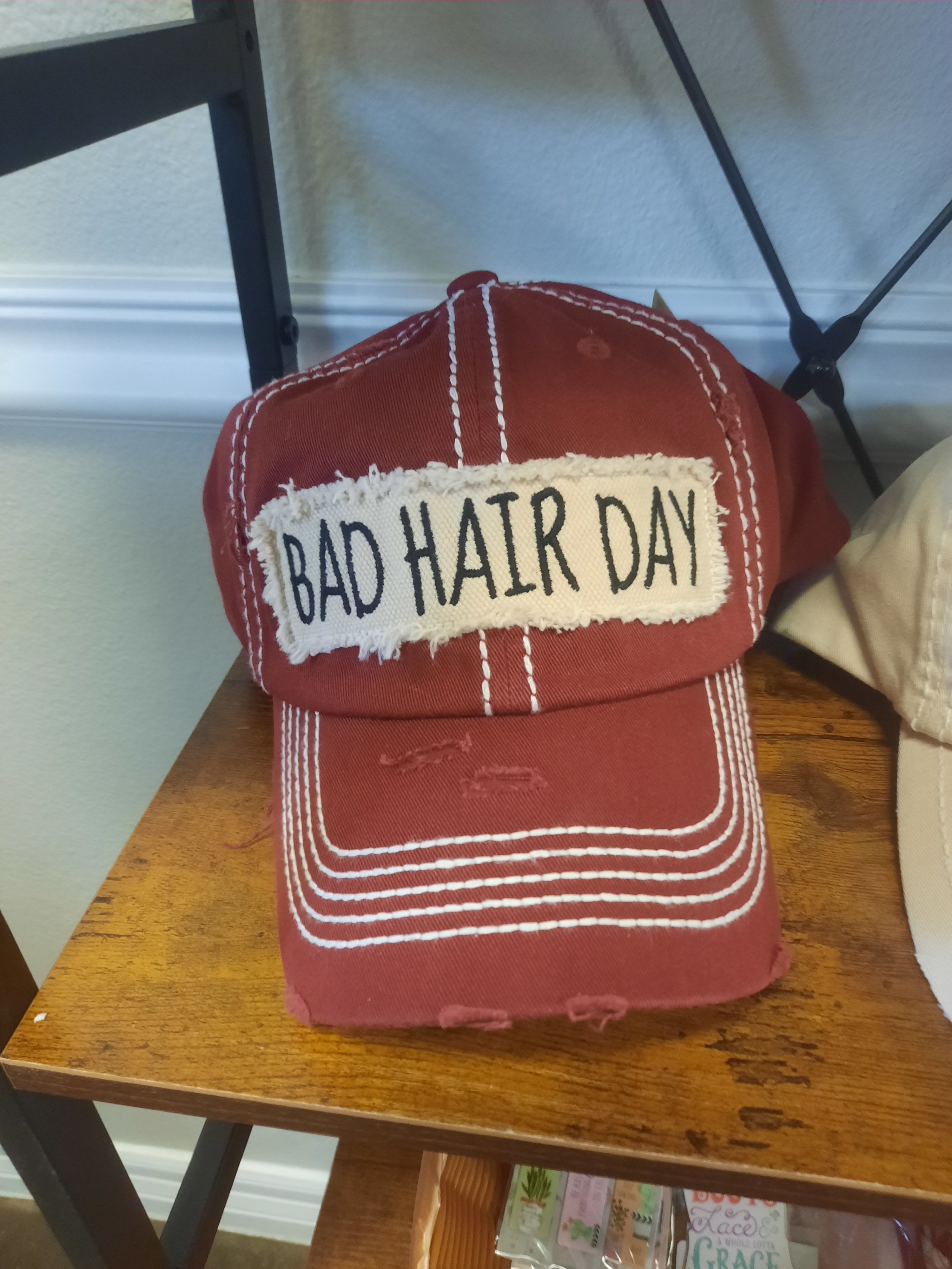 Bad Hair Day - Ballcap - A playful, casual pick for the person who prefers humor over formality - this novelty "Bad Hair Day" ballcap makes a fun gift for birthdays, graduation parties, or just because. As a gift item or personal accessory, the red baseball cap with white contrast stitching and a frayed fabric patch that reads "BAD HAIR DAY" in black lettering sends a lighthearted, relatable message that will make the recipient smile.  The cap has a worn-in, slightly distressed look with a relaxed everyday fit rather than a polished fashion statement. The red, white, and black colorway keeps the design bold and versatile, while the rectangular frayed patch adds texture and a handcrafted feel. Sized like a standard baseball cap, it's an easy, low-maintenance accessory that arrives ready to wear and pairs well with casual wardrobes - a cheeky, effortless way to brighten someone's day.