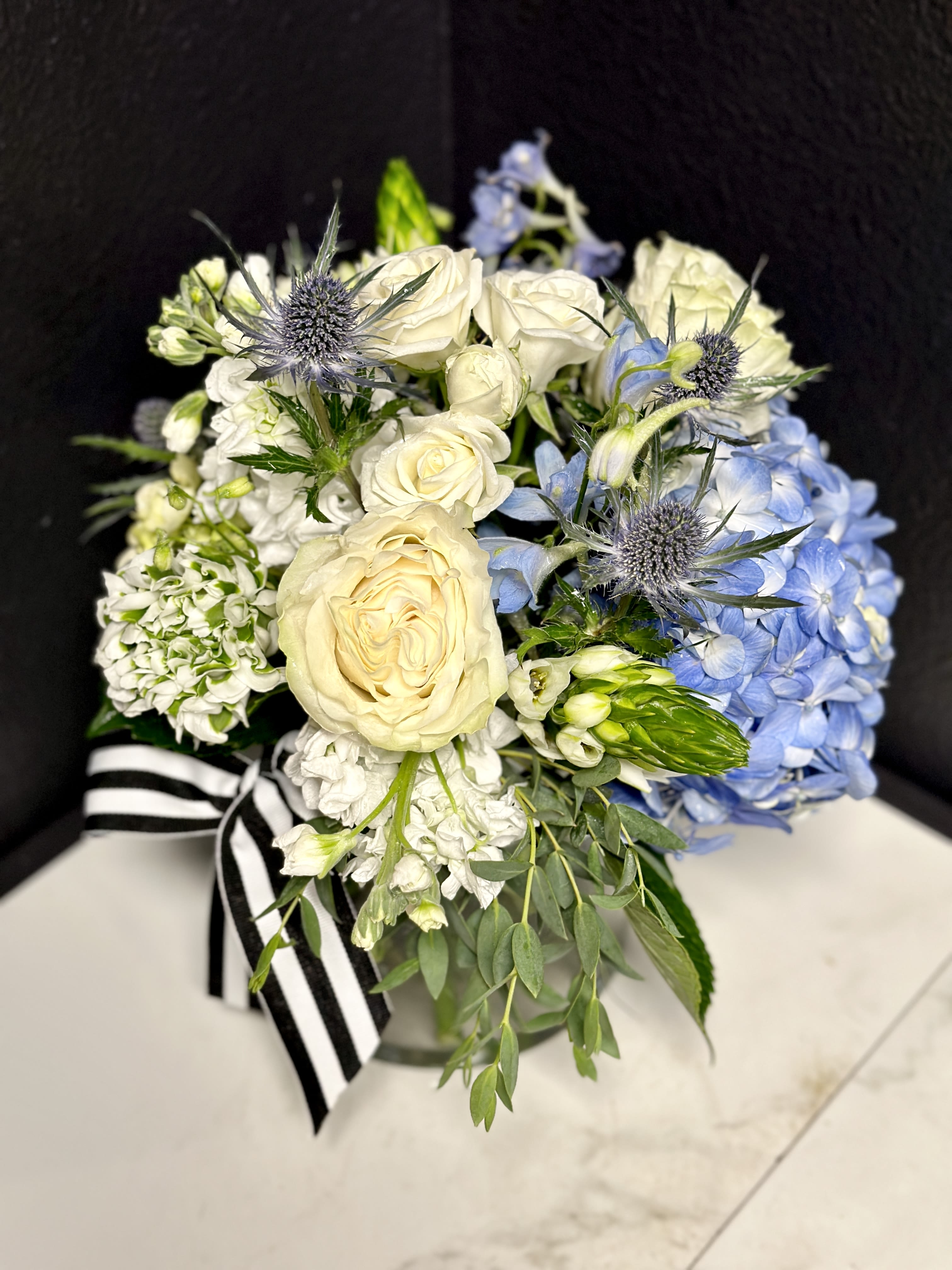 Bouquet of white roses and blue hydrangeas with thistle accents