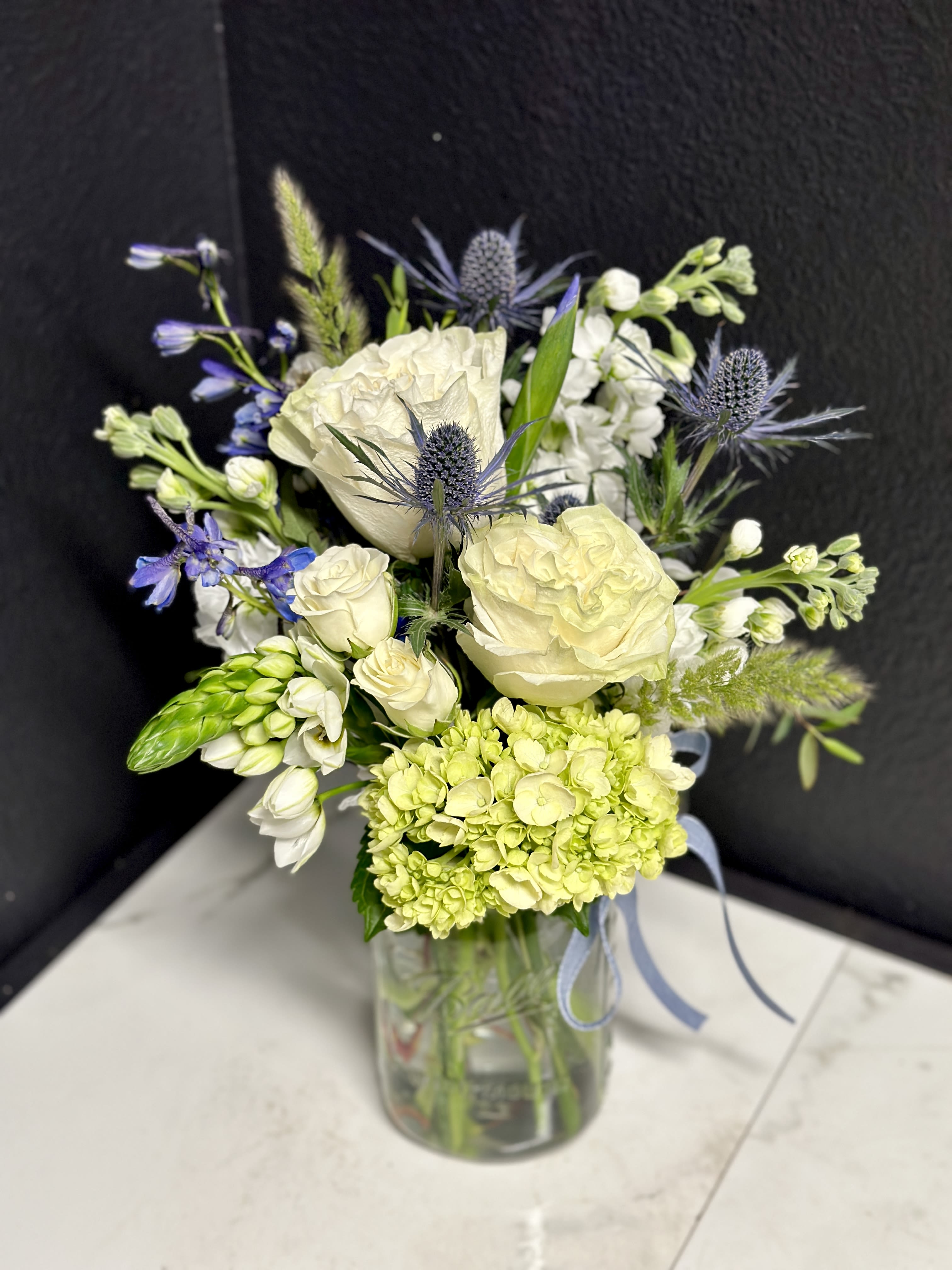 White and pale green bouquet with blue accents in a glass vase