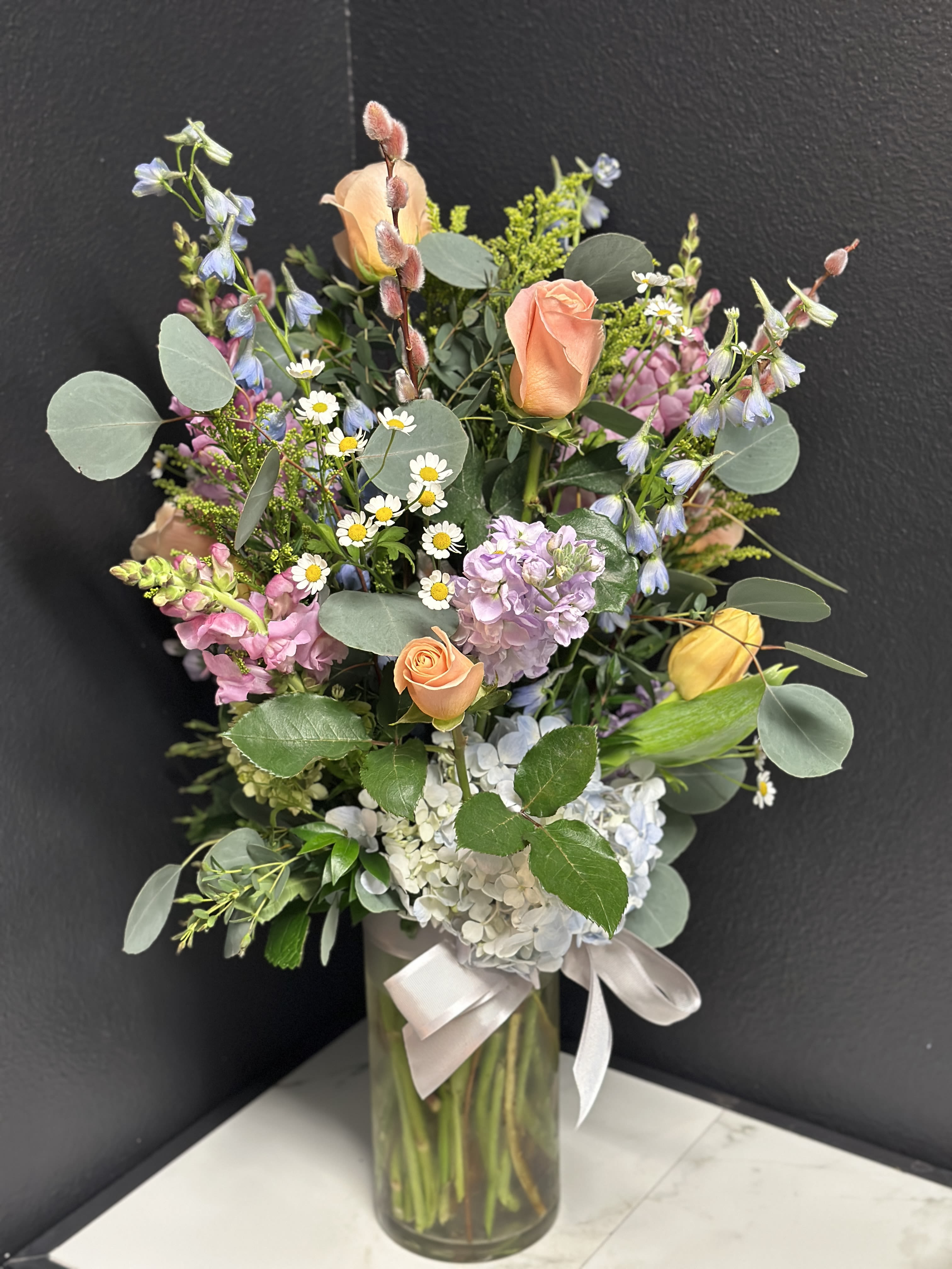 Tall Soft Garden - A tall elegant designer's choice garden of our prettiest seasonal pastel blossoms &amp; foliage. Arranged in a clear glass vase. Approximately 24"H x 15"W  PICTURED AS DELUXE Floral varieties may vary but will be of similar quality and style.  