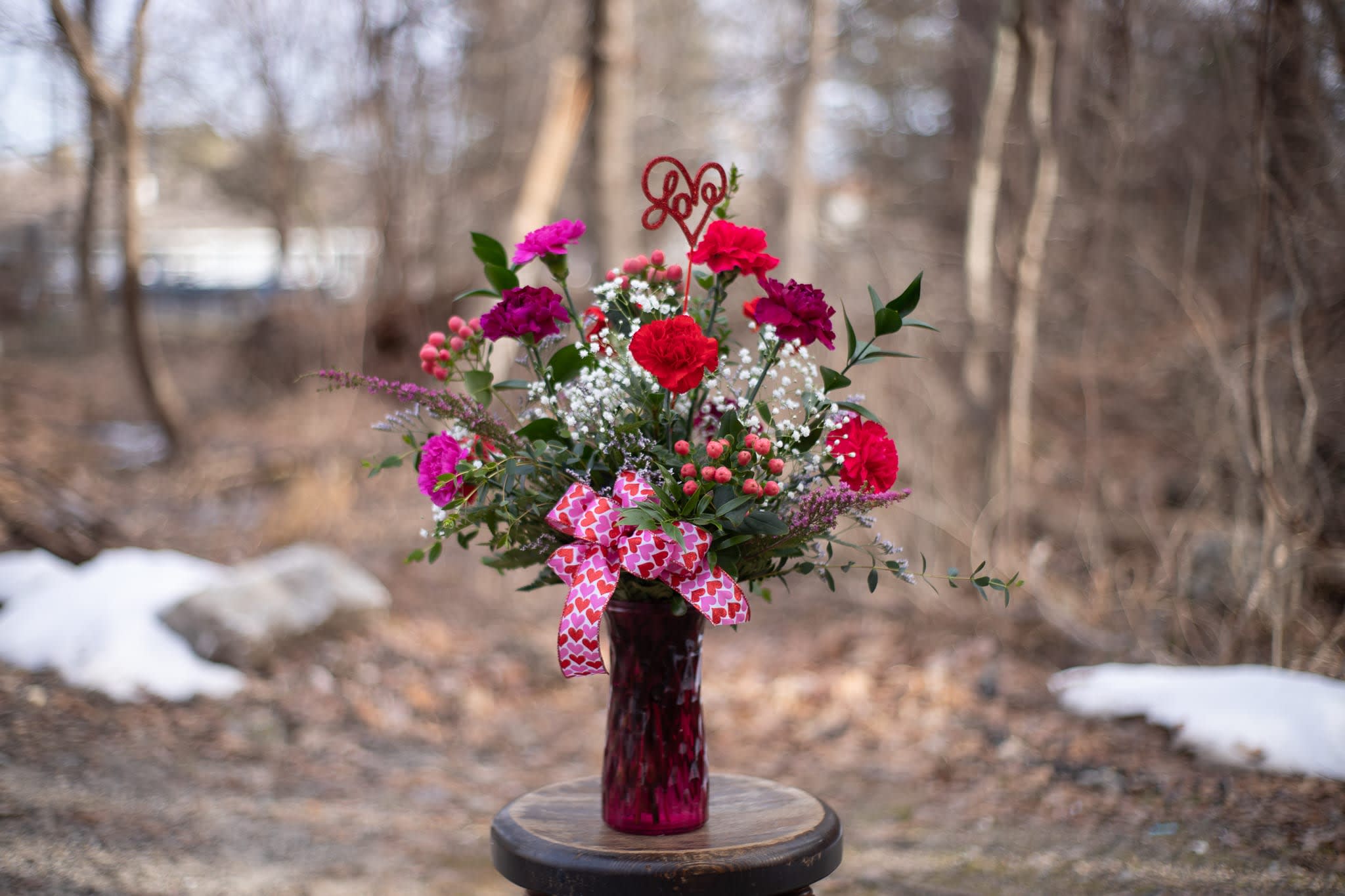 Pink and red carnation bouquet in a glass vase with a heart ribbon