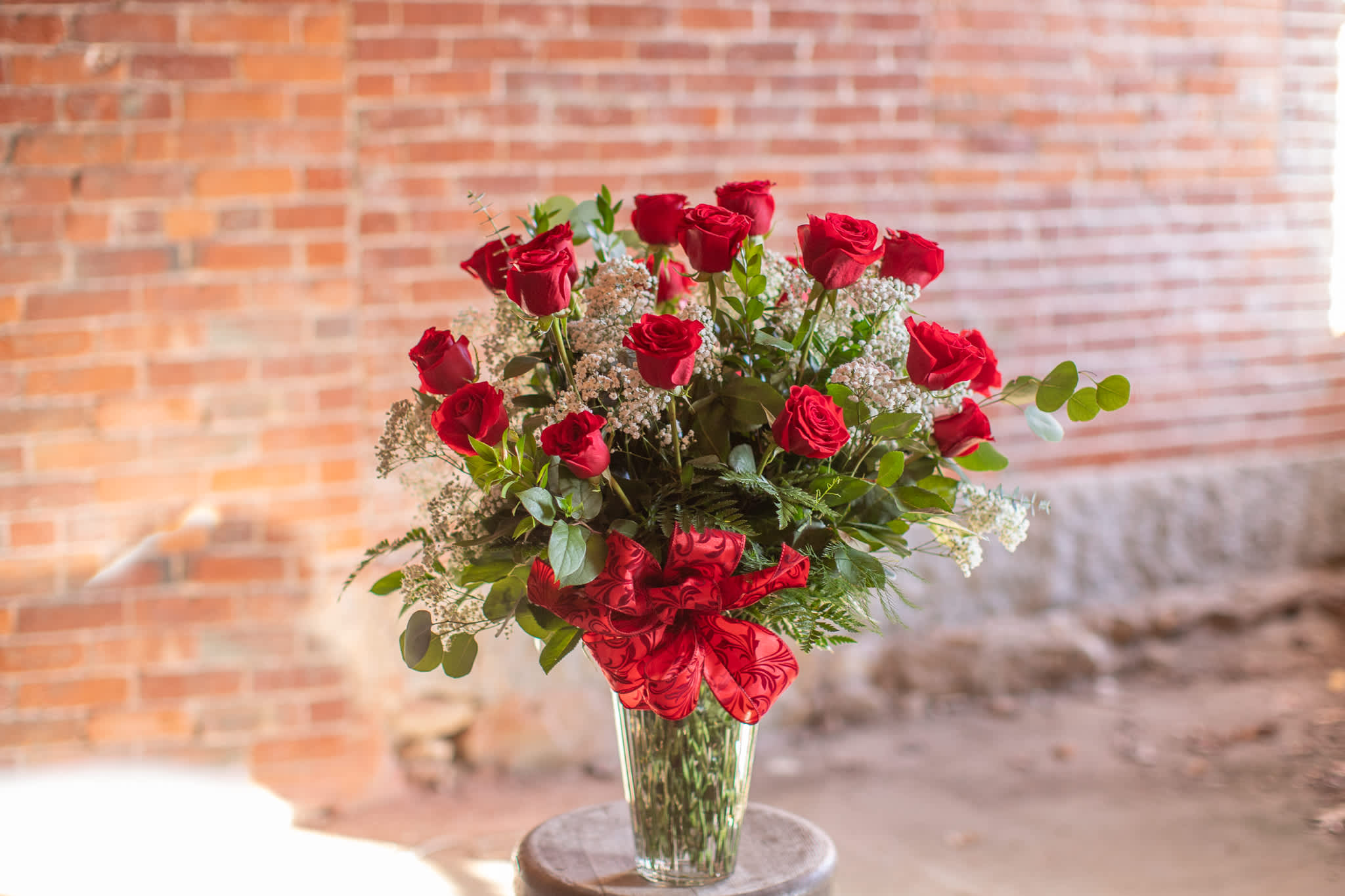 Red roses arranged in a clear glass vase with a red ribbon
