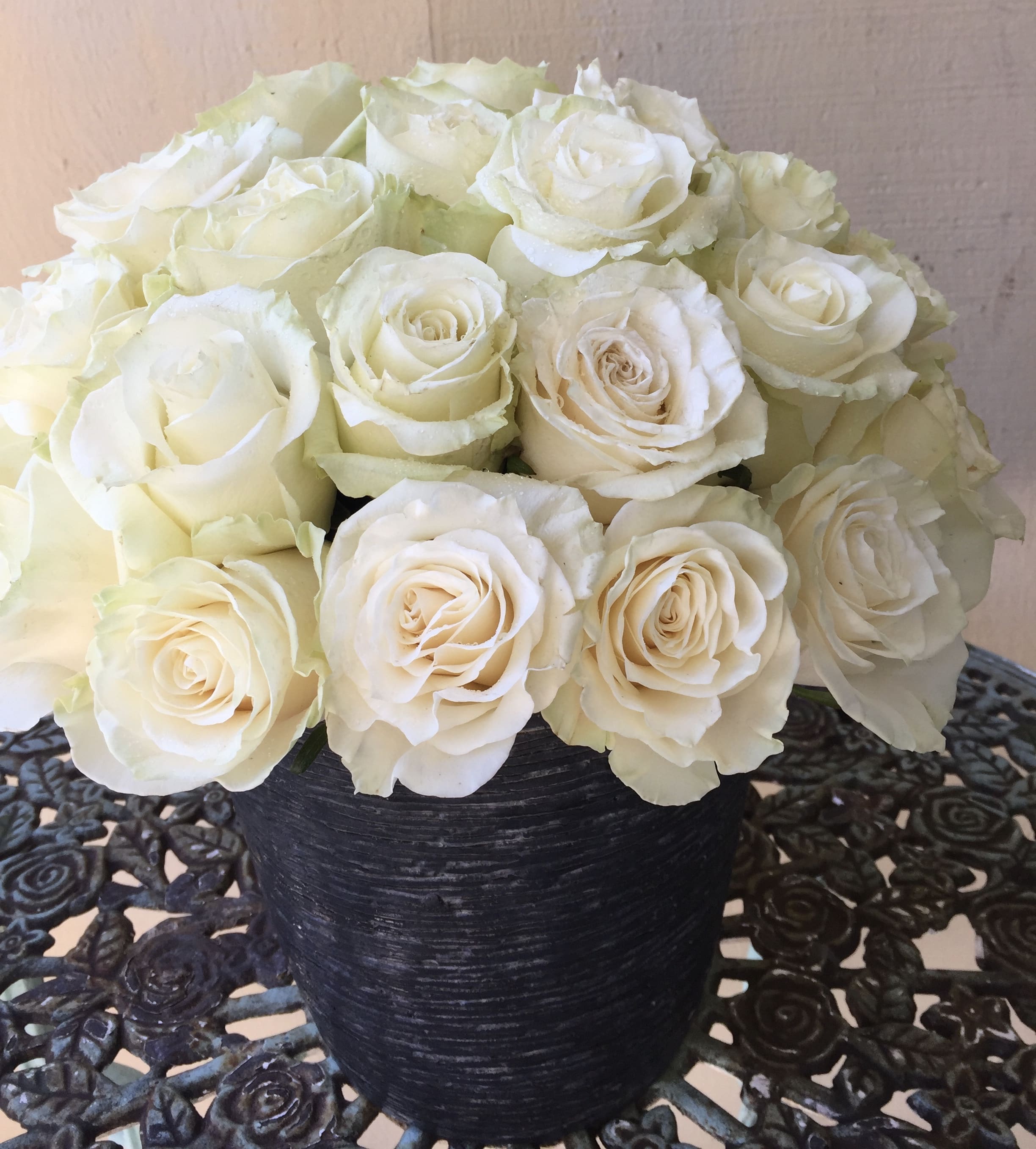 Compact arrangement of ivory roses in a black textured vase