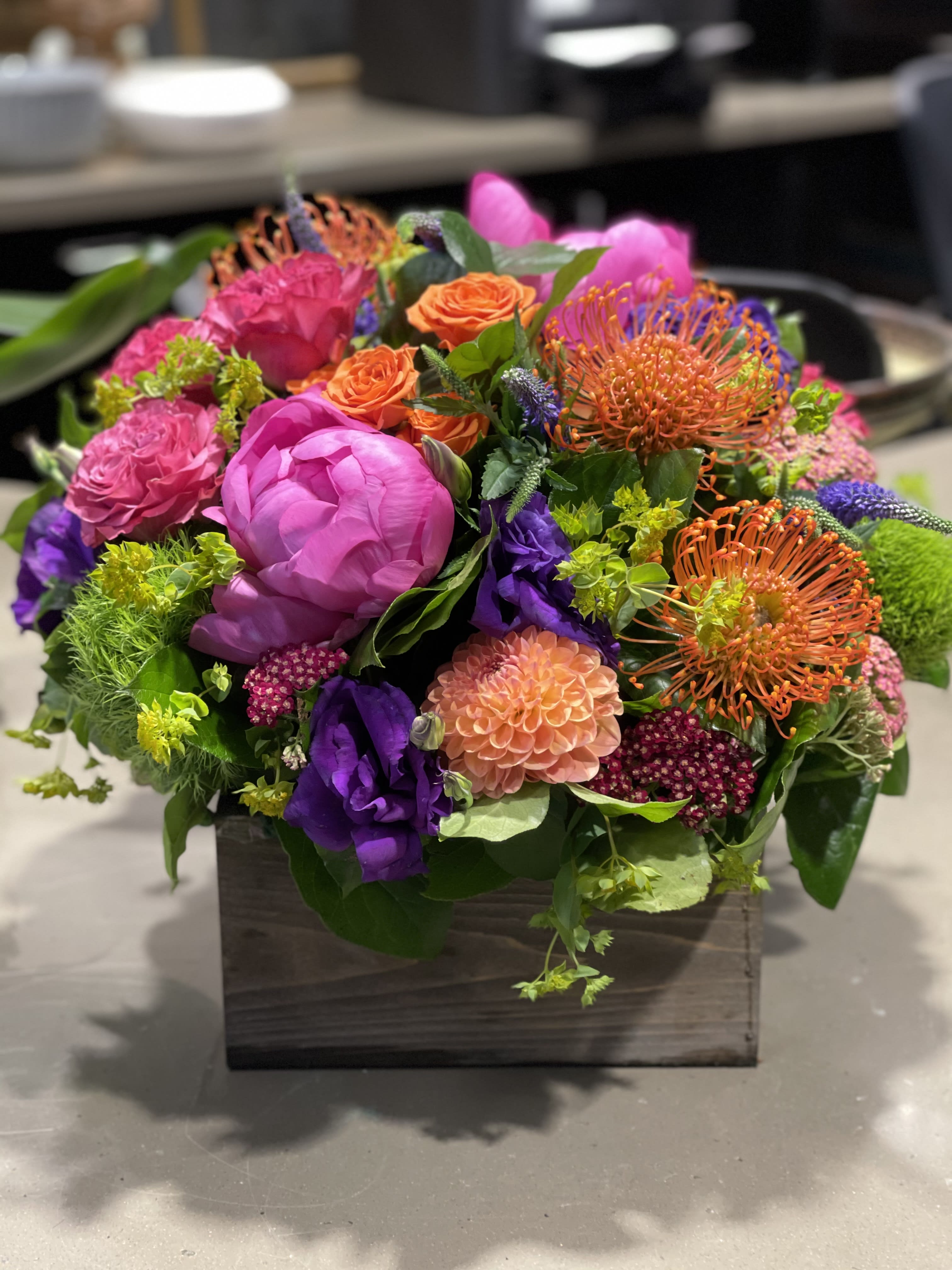 Bright mixed arrangement of pink, orange, purple, and green flowers in a low wooden box