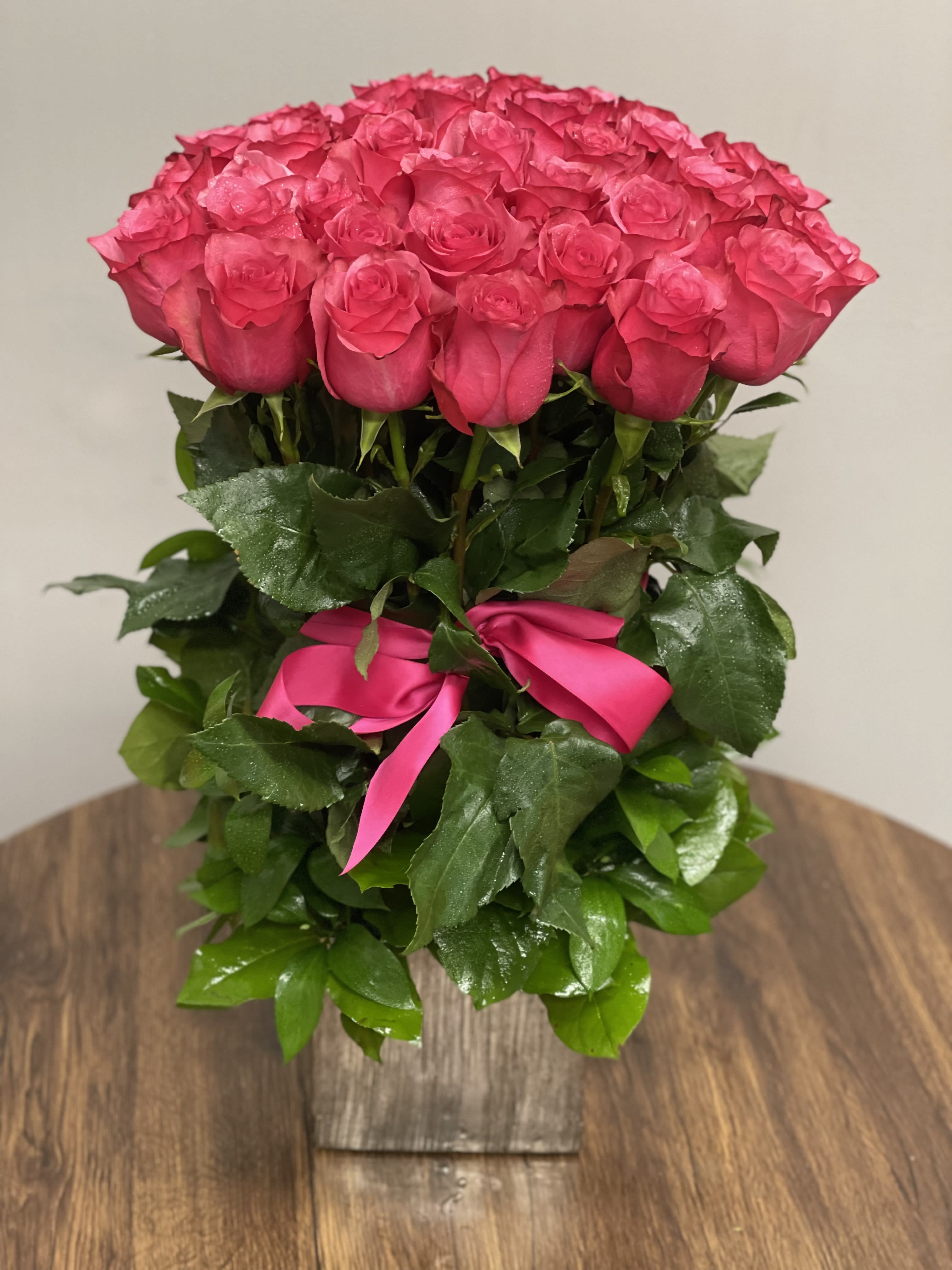 Tall arrangement of bright pink roses with a matching ribbon in a rustic wooden vase
