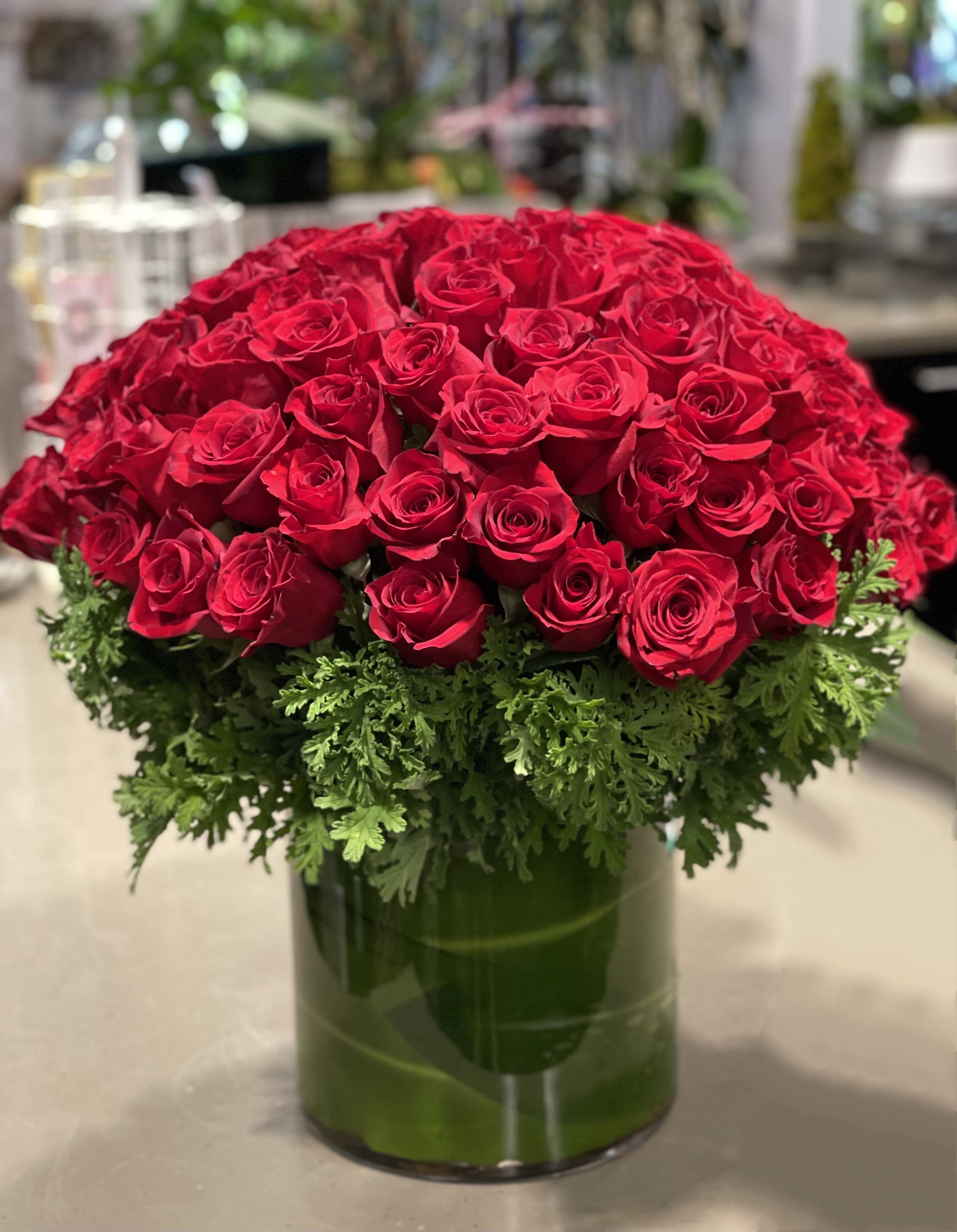 Large dome of red roses with a green foliage collar in a clear glass cylinder vase.