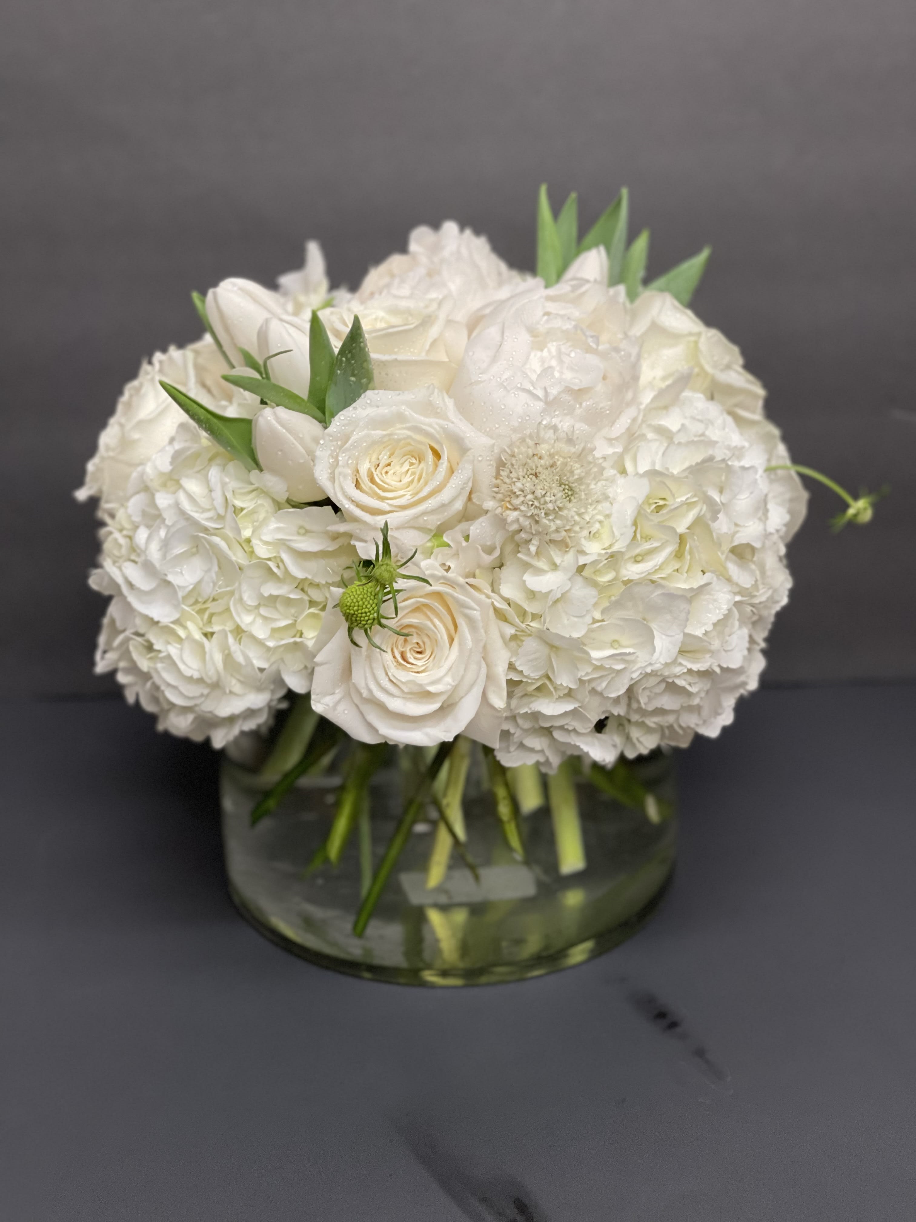 Low round arrangement of white roses, hydrangeas, and peonies in a clear glass vase