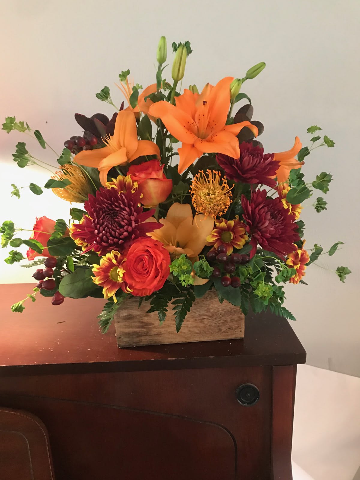 Orange lilies and red chrysanthemums in a wooden box arrangement