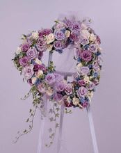 Lavender and white floral wreath on a stand with trailing greenery