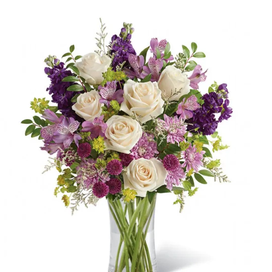 Bouquet of white roses and purple flowers in a clear glass vase