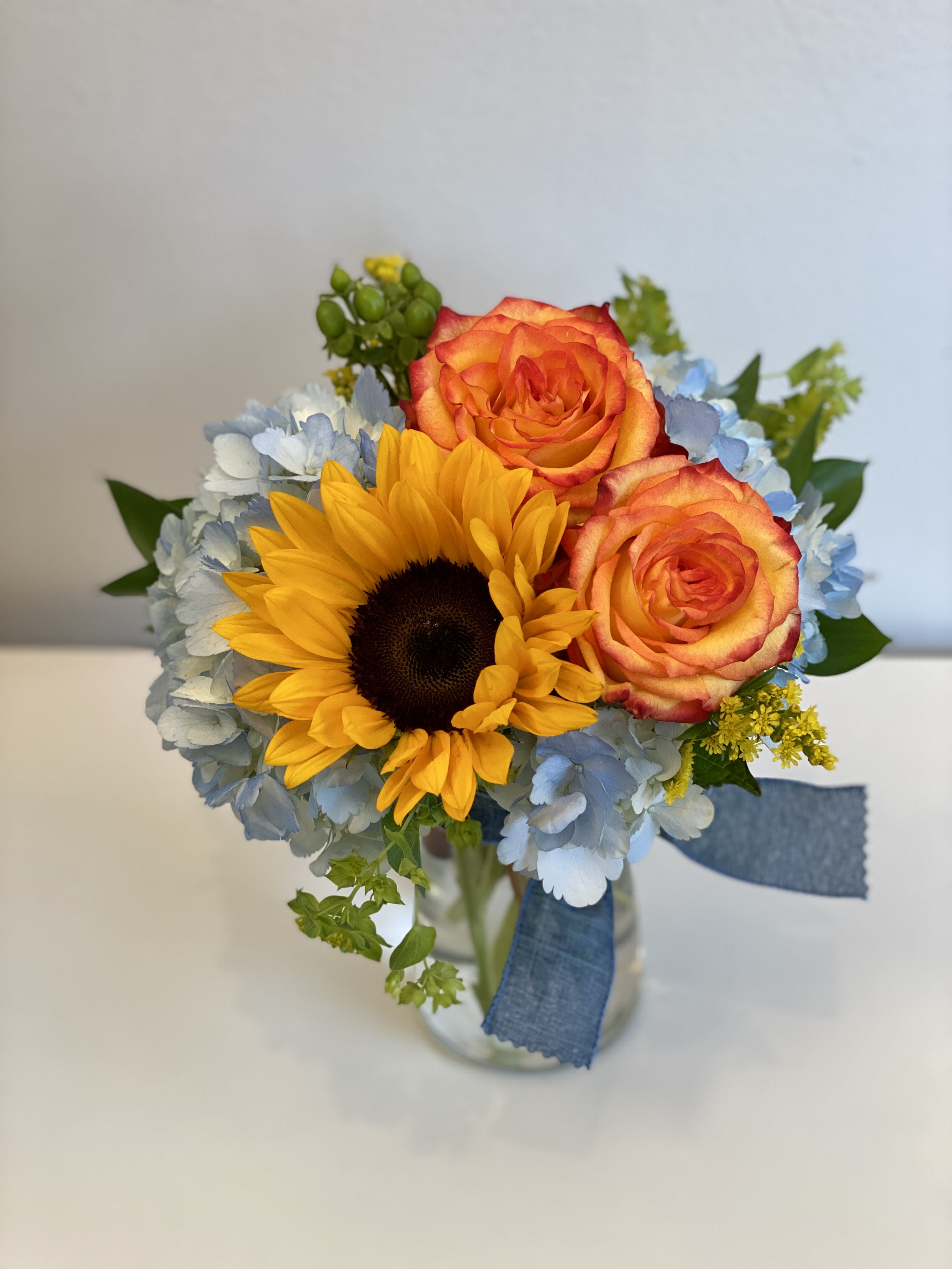 Bouquet of sunflowers, orange roses, and blue hydrangeas in a glass vase
