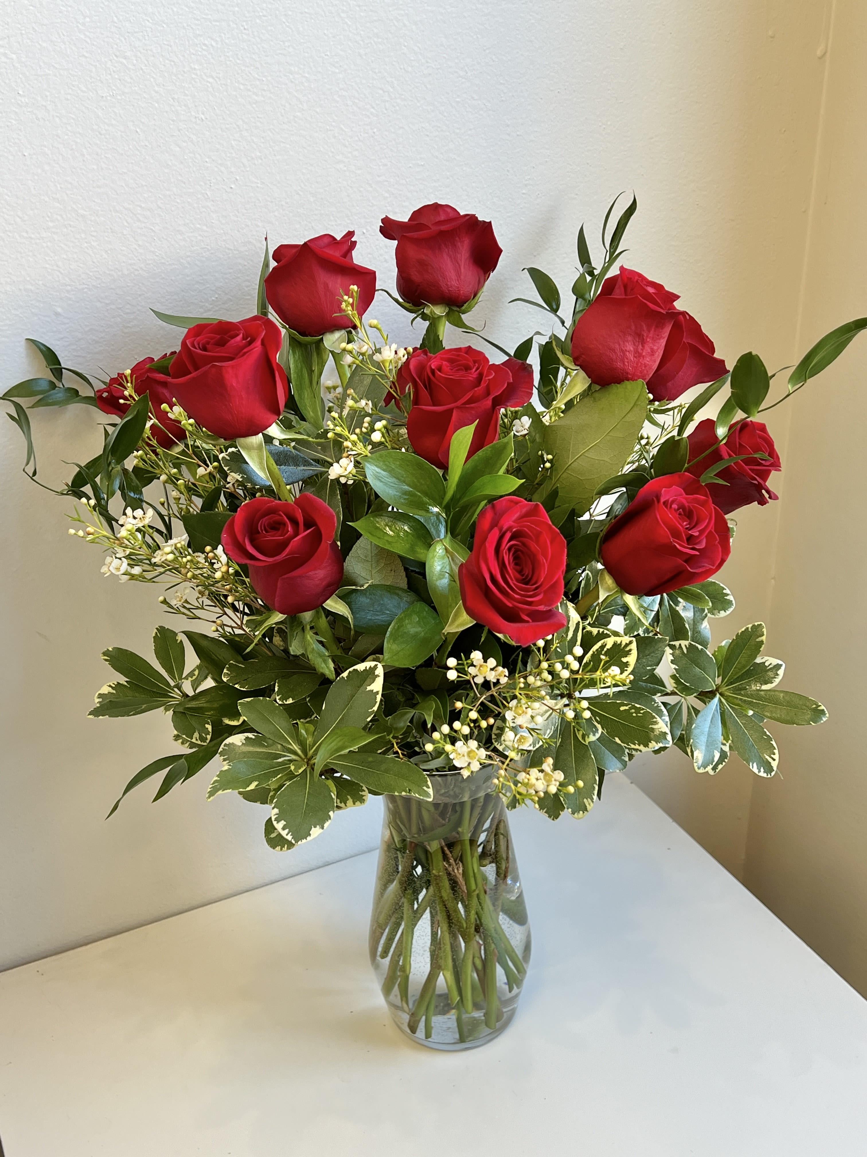 Red roses arranged in a clear glass vase with mixed greenery