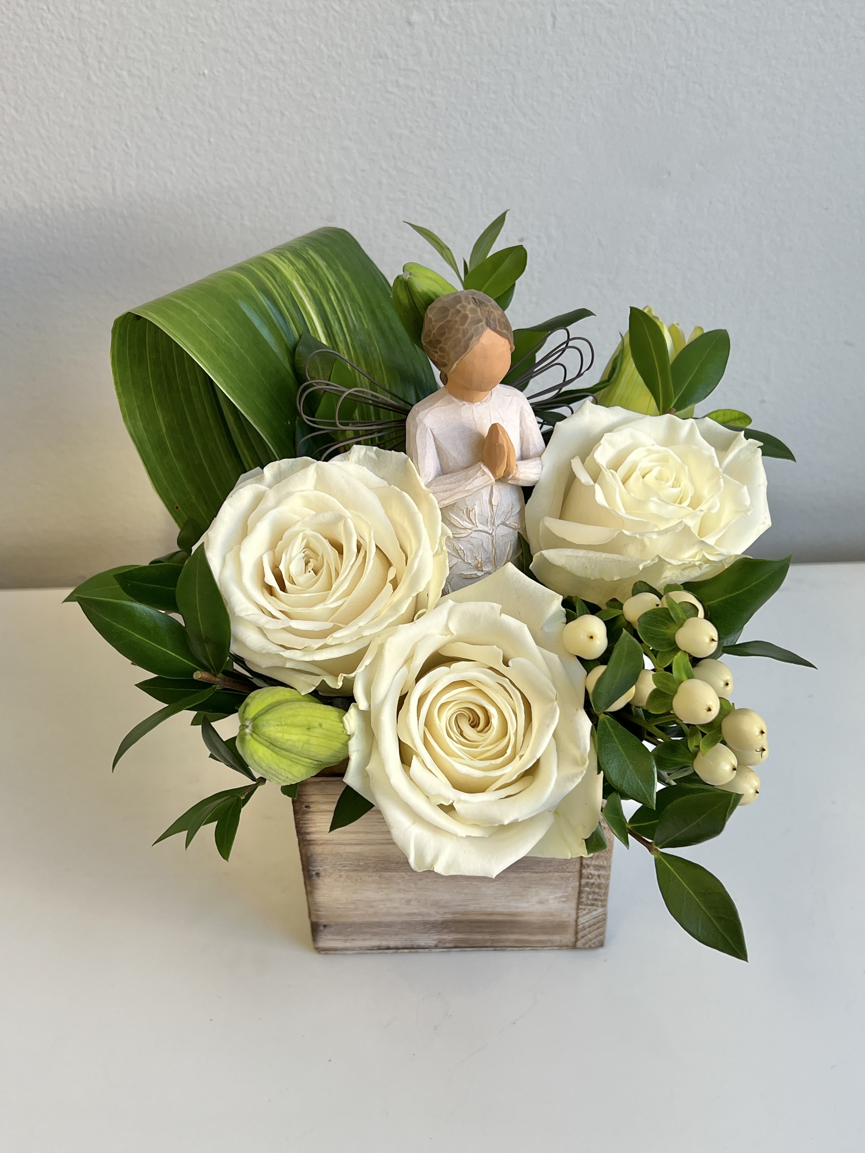 White roses in a wooden box with a small angel figurine