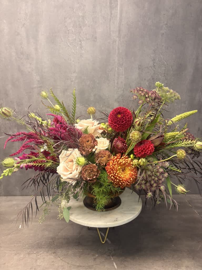 Large mixed floral arrangement in a dark vase with cream, red, and orange blooms