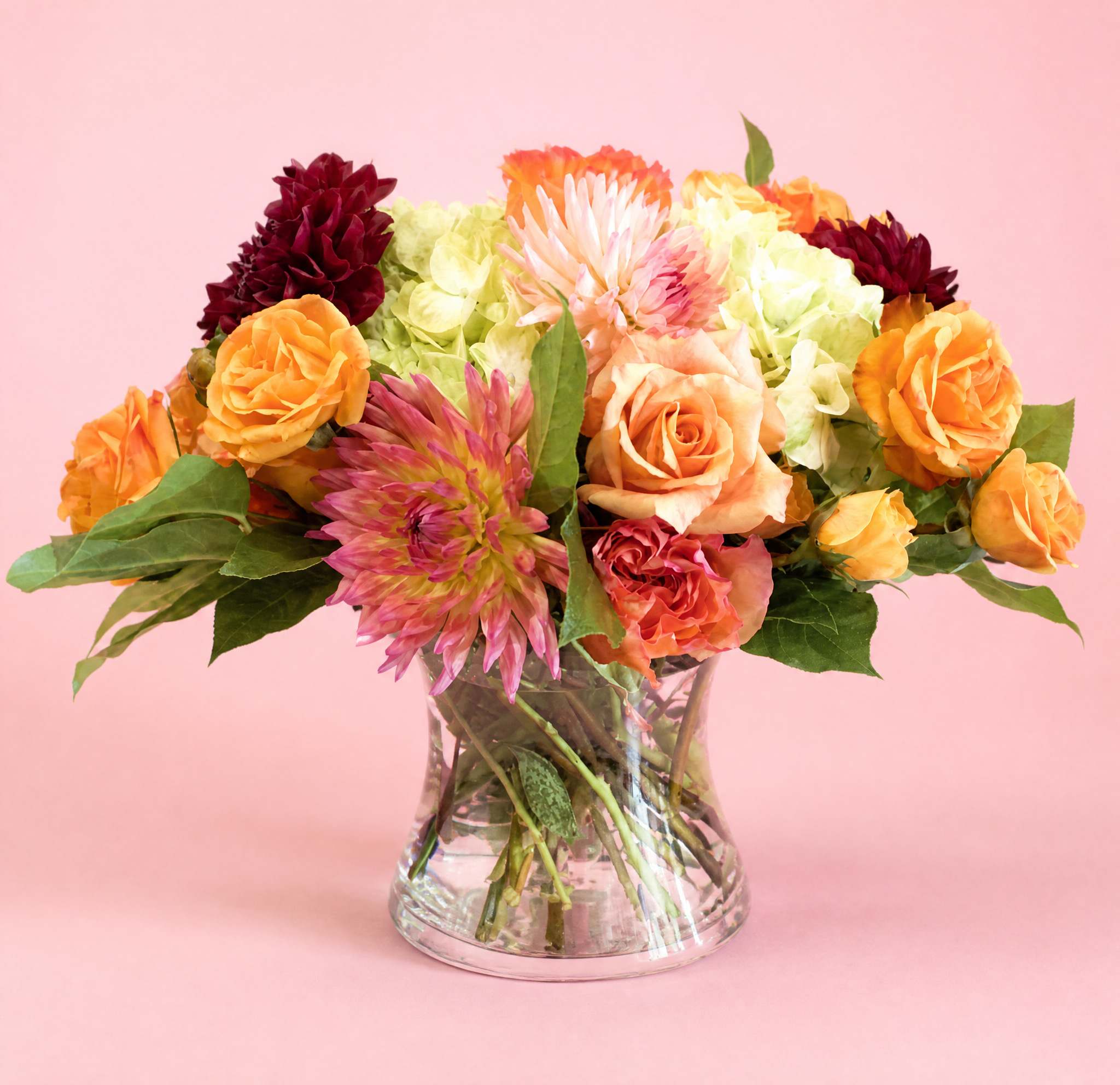 Mixed bouquet of orange, pink, and burgundy flowers in a clear glass vase
