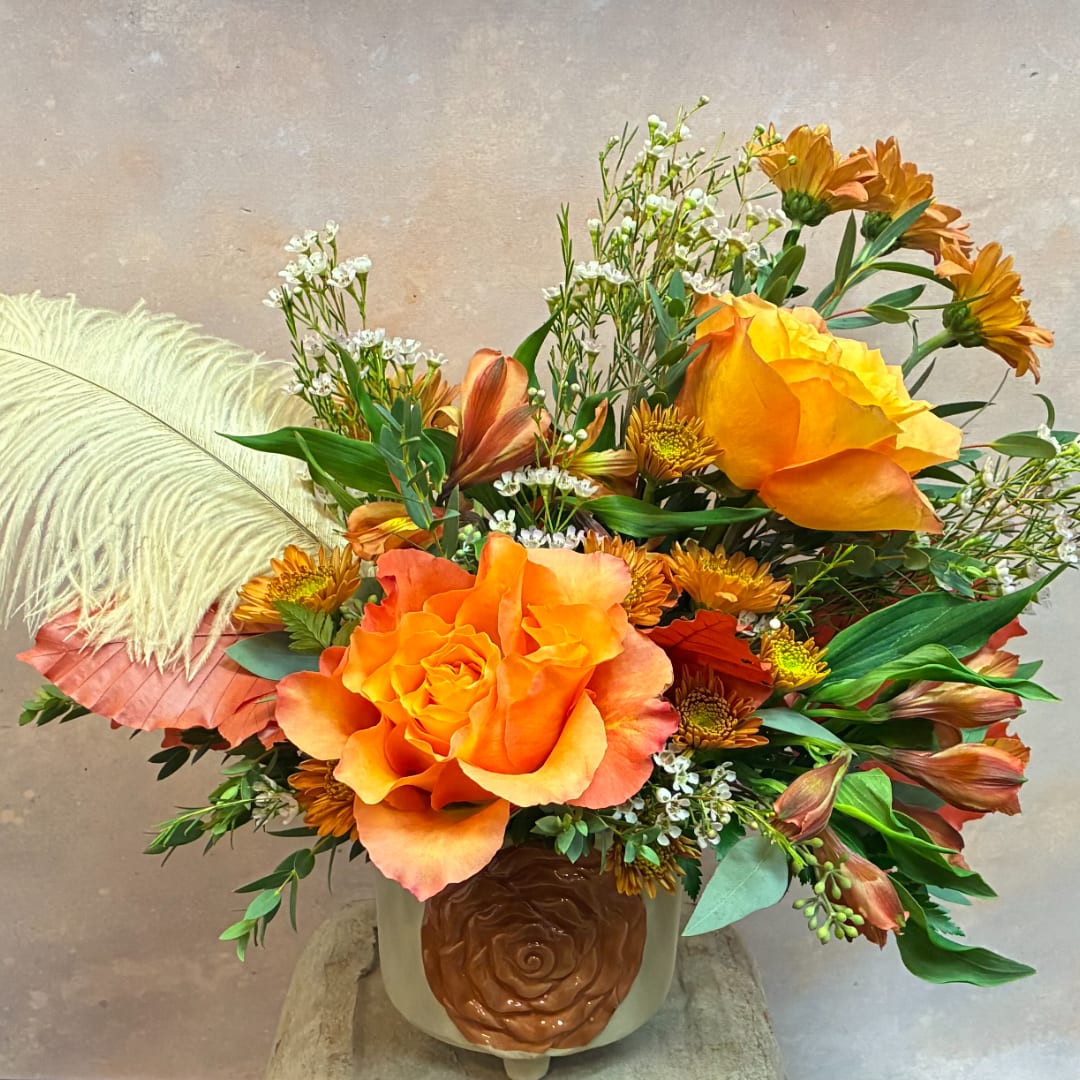 Orange roses and mixed blooms in a ceramic vase with a rose emblem