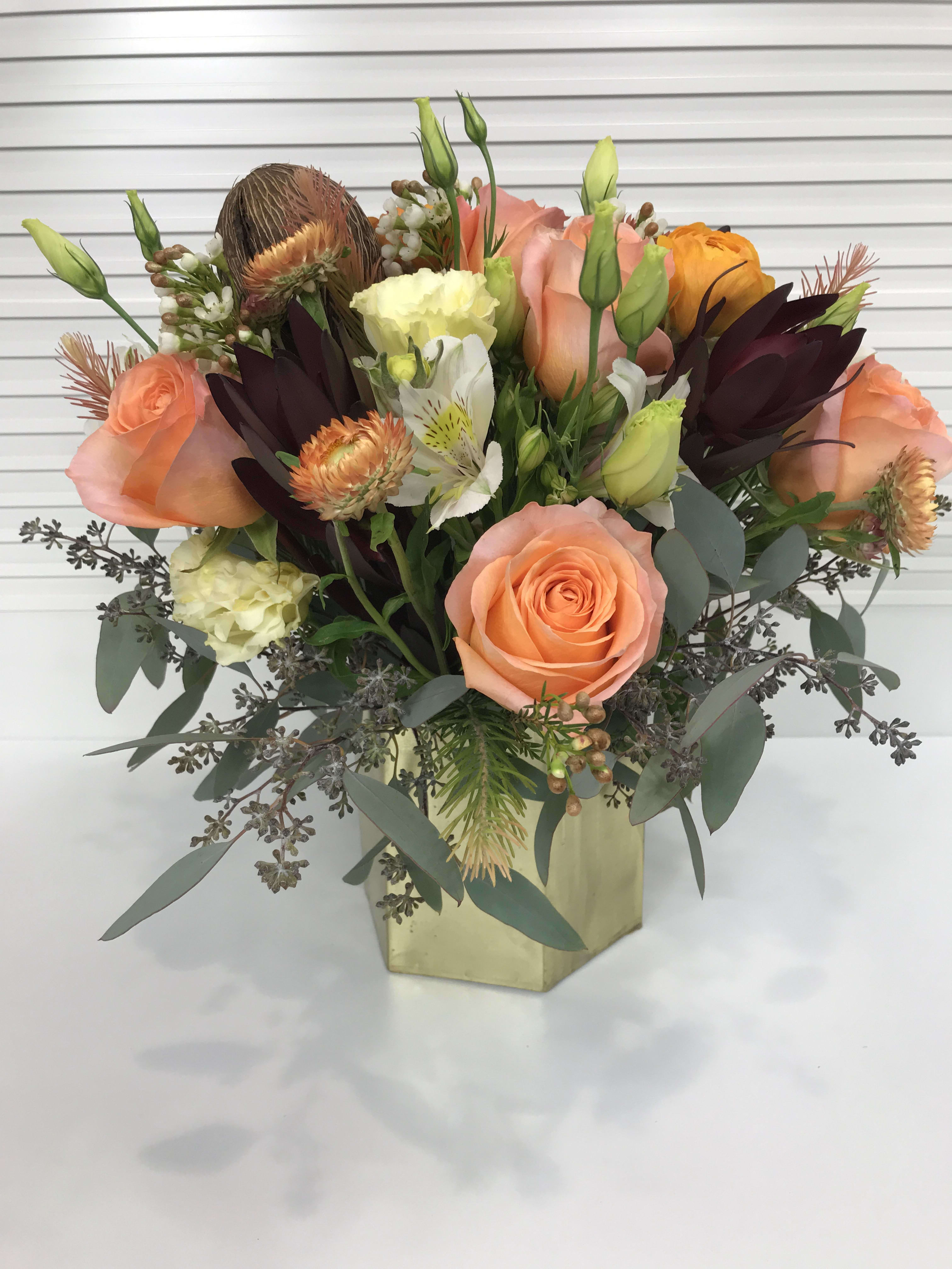 A Splash of Glam - Collection of peach colored roses, ranunculus, alstroemeria, Lisianthus, wax flowers, and more, in a contemporary gold vase