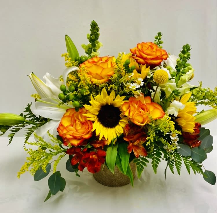 Bouquet of orange roses, sunflowers, and white lilies in a burlap-wrapped container