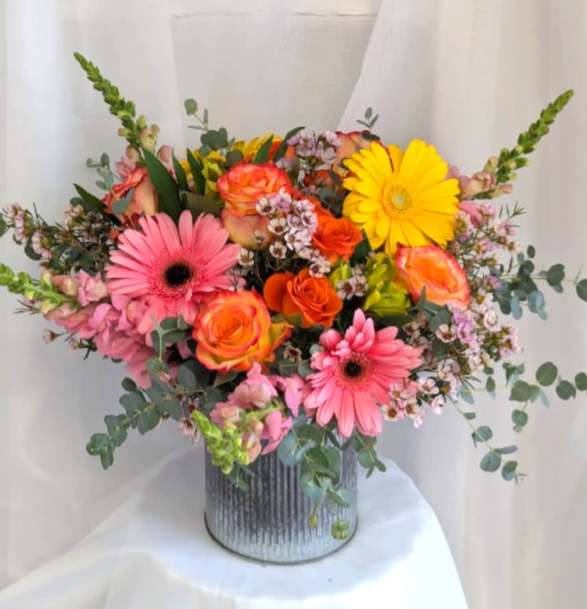 Bright arrangement of pink gerbera daisies, orange roses, and yellow blooms in a ribbed metal vase