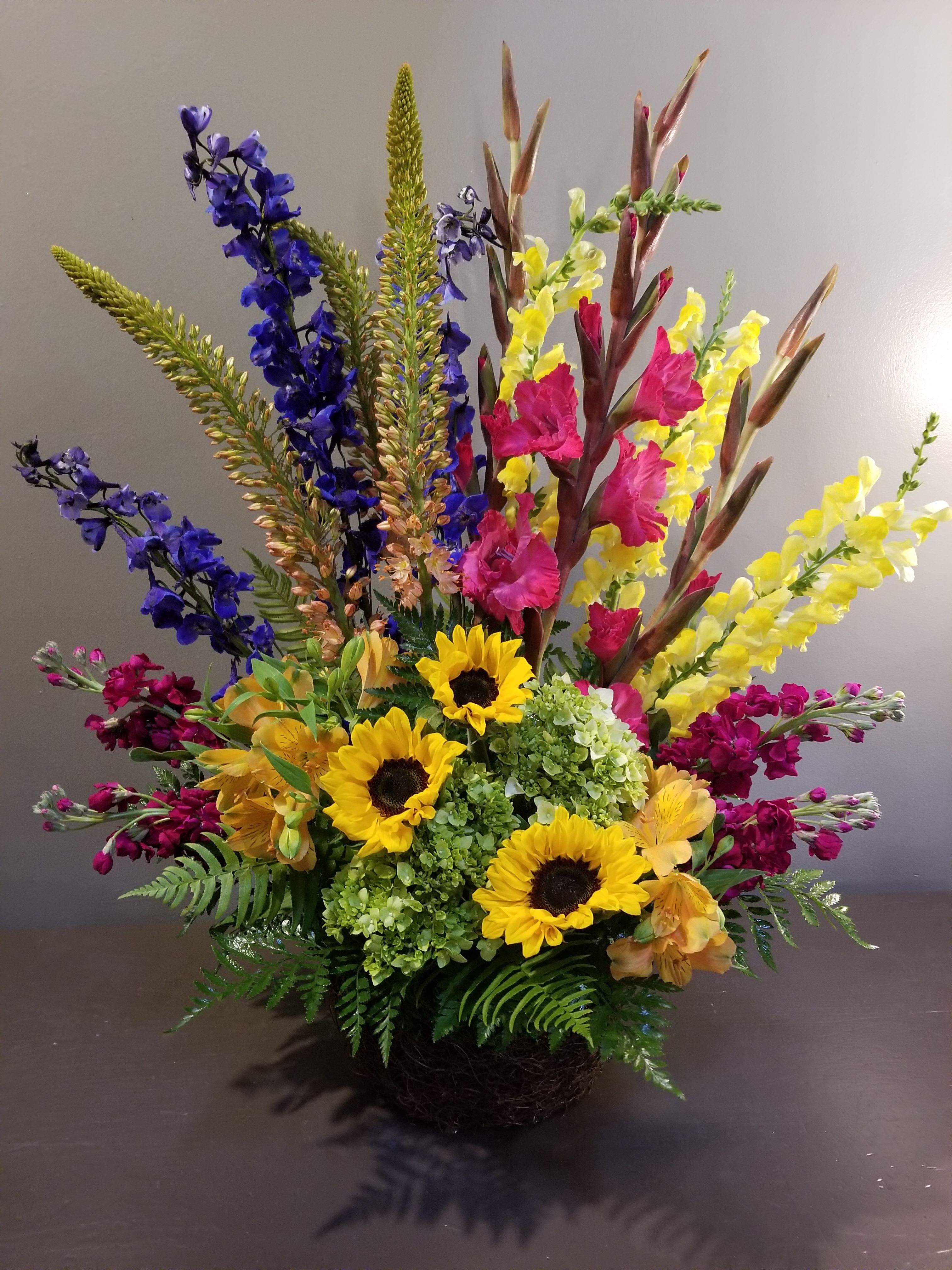 Colorful mixed flower arrangement with sunflowers, snapdragons, and hydrangeas in a basket