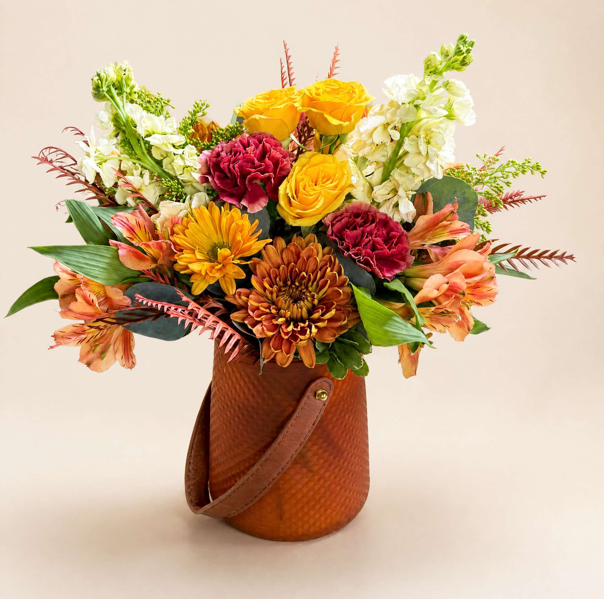 Mixed bouquet of yellow roses, carnations, chrysanthemums, and white blooms in a brown handled container